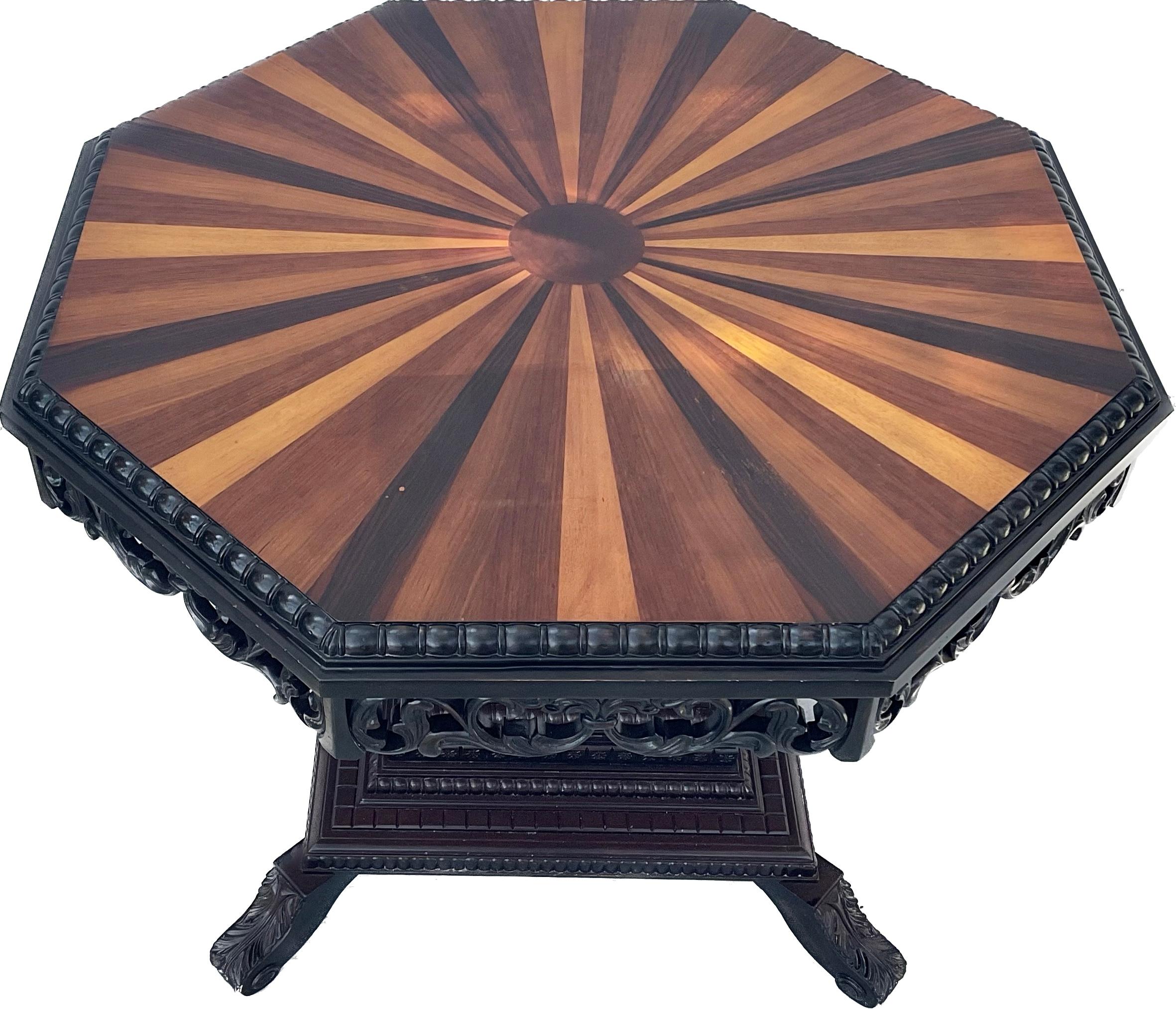 Very unique late 20th century Anglo-Indian octagonal center table in ebony wood. Table has segmented wood top, inlaid with rays of exotic woods.  Carved frieze is supported by wooden columns on a square with shaped bracket feet. This magnificent