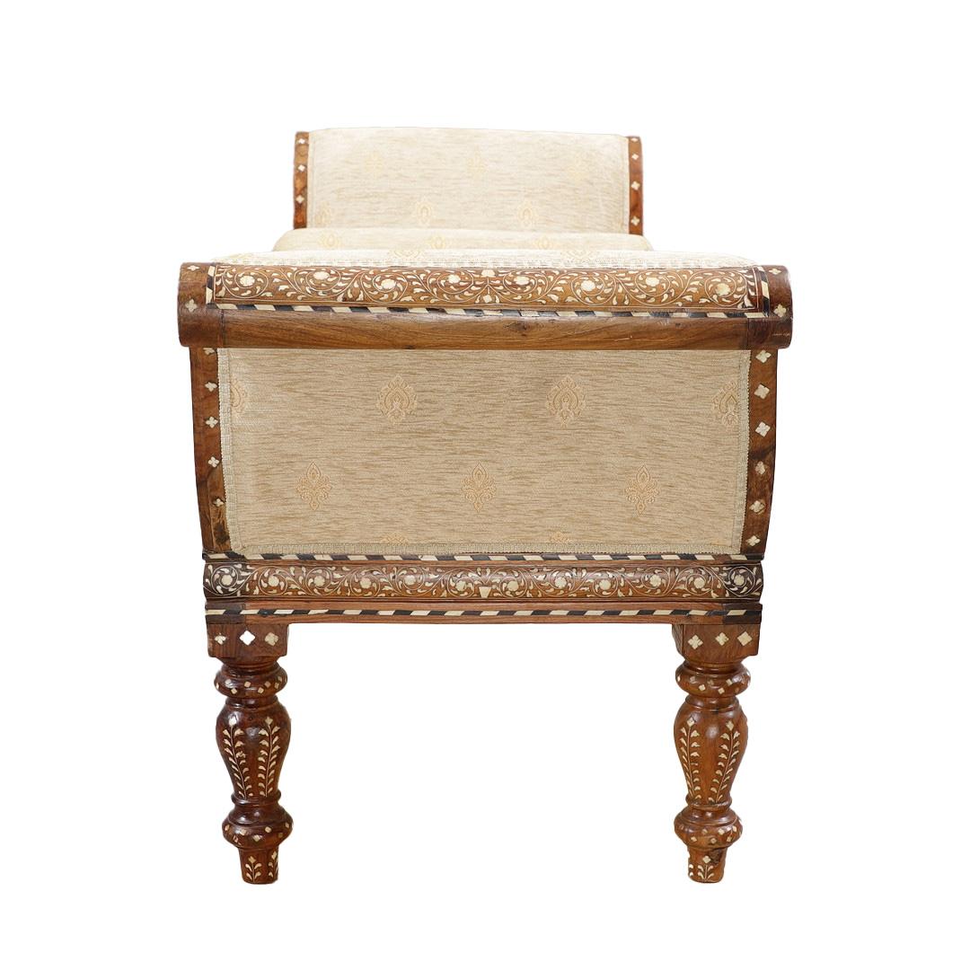 Banc anglo-indien aux côtés incurvés, dont l'assise et les côtés sont recouverts d'un rembourrage serré, soutenu par quatre pieds tournés. Le cadre en bois dur de couleur bois de fruitier incrusté de motifs géométriques en composition simulant l'os,