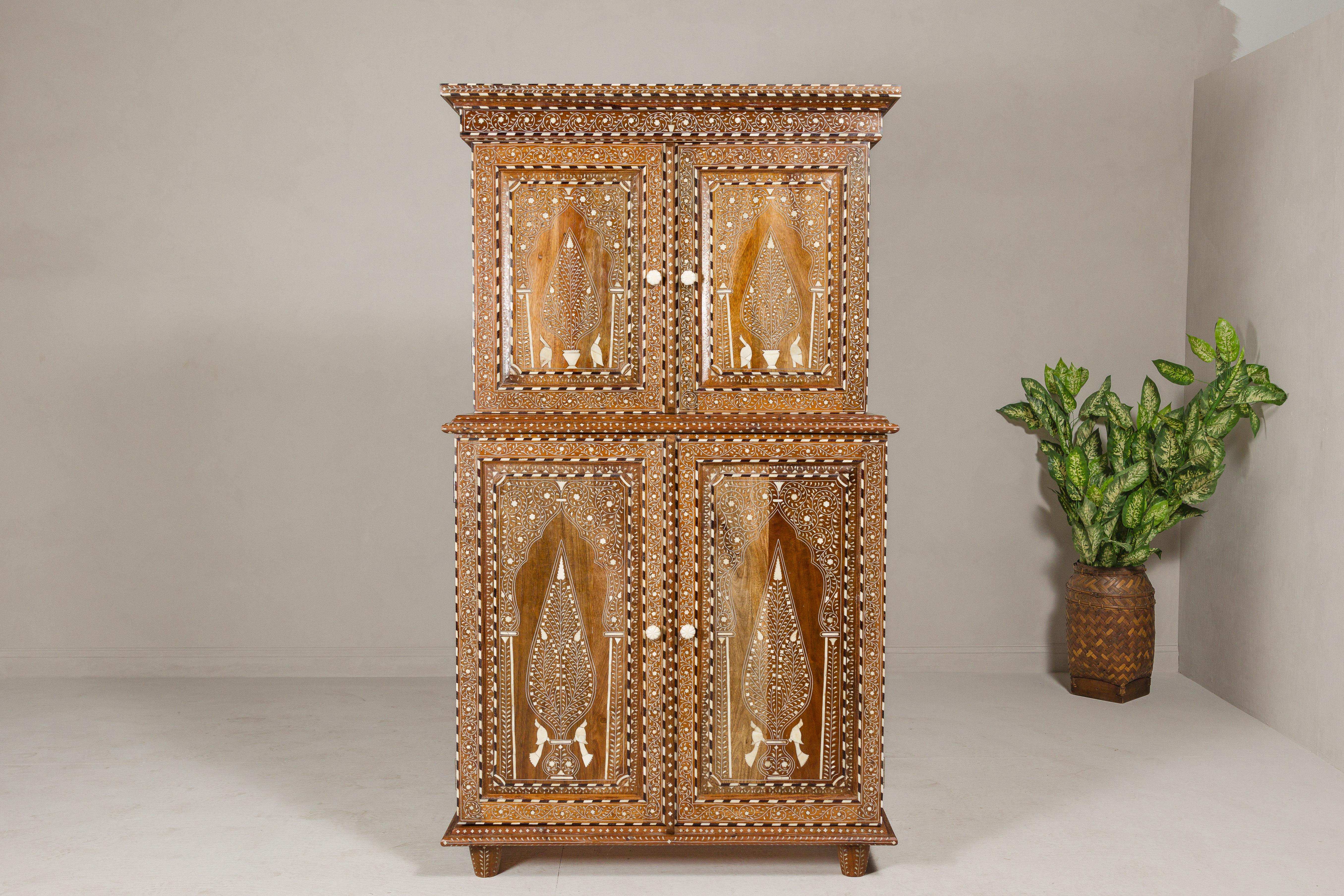 An Anglo-Indian style two part mango wood buffet à deux-corps with four doors, floral and bird themed bone inlaid décor, and flaming patterns on the doors. This Anglo-Indian style mango wood buffet à deux-corps is an opulent masterpiece that