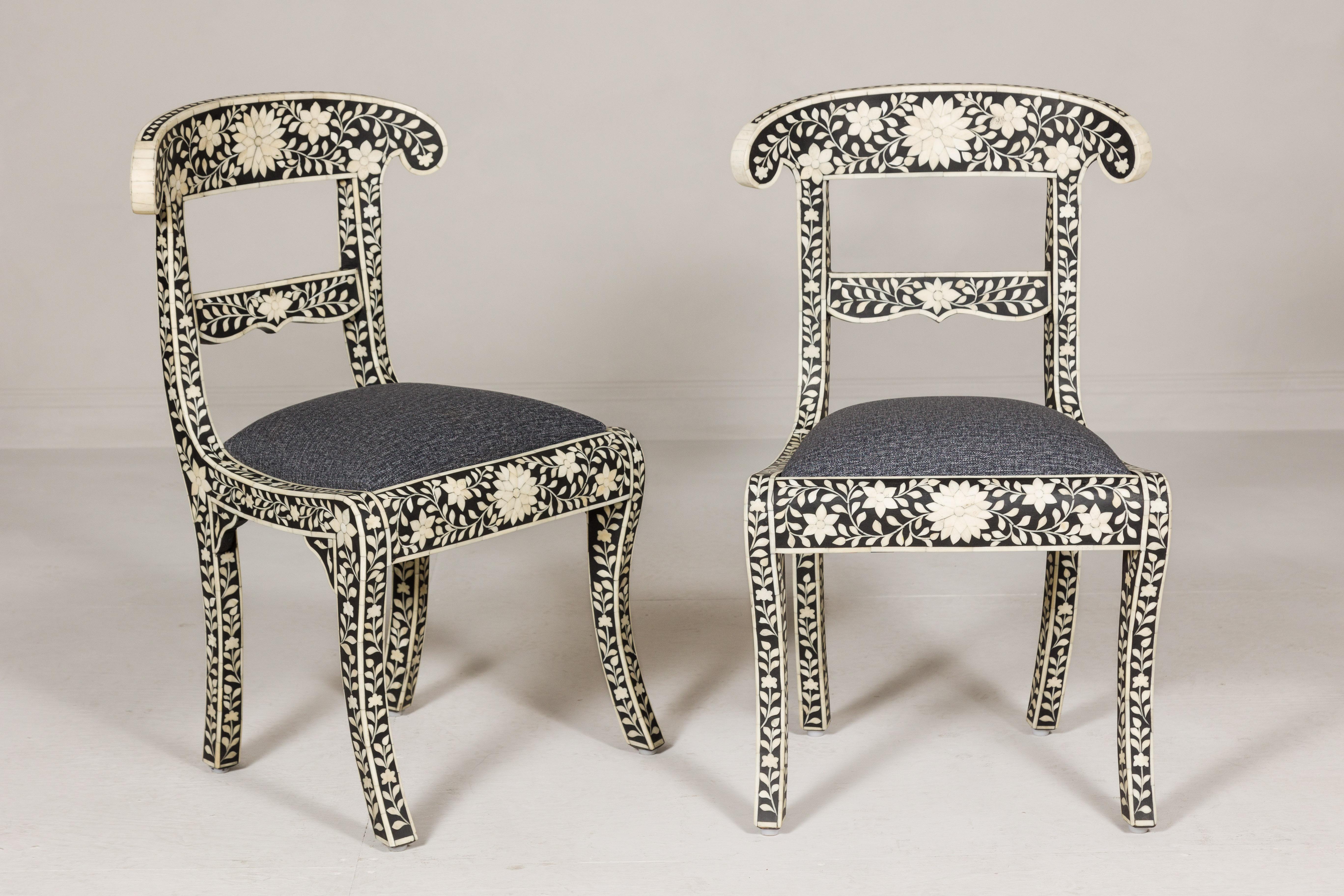A pair of Anglo-Indian style mango wood side chairs with floral-themed bone inlaid décor, dark grey fabric and saber legs. Unveil a fusion of Eastern allure and Western design with this pair of Anglo-Indian style mango wood side chairs. Nestled