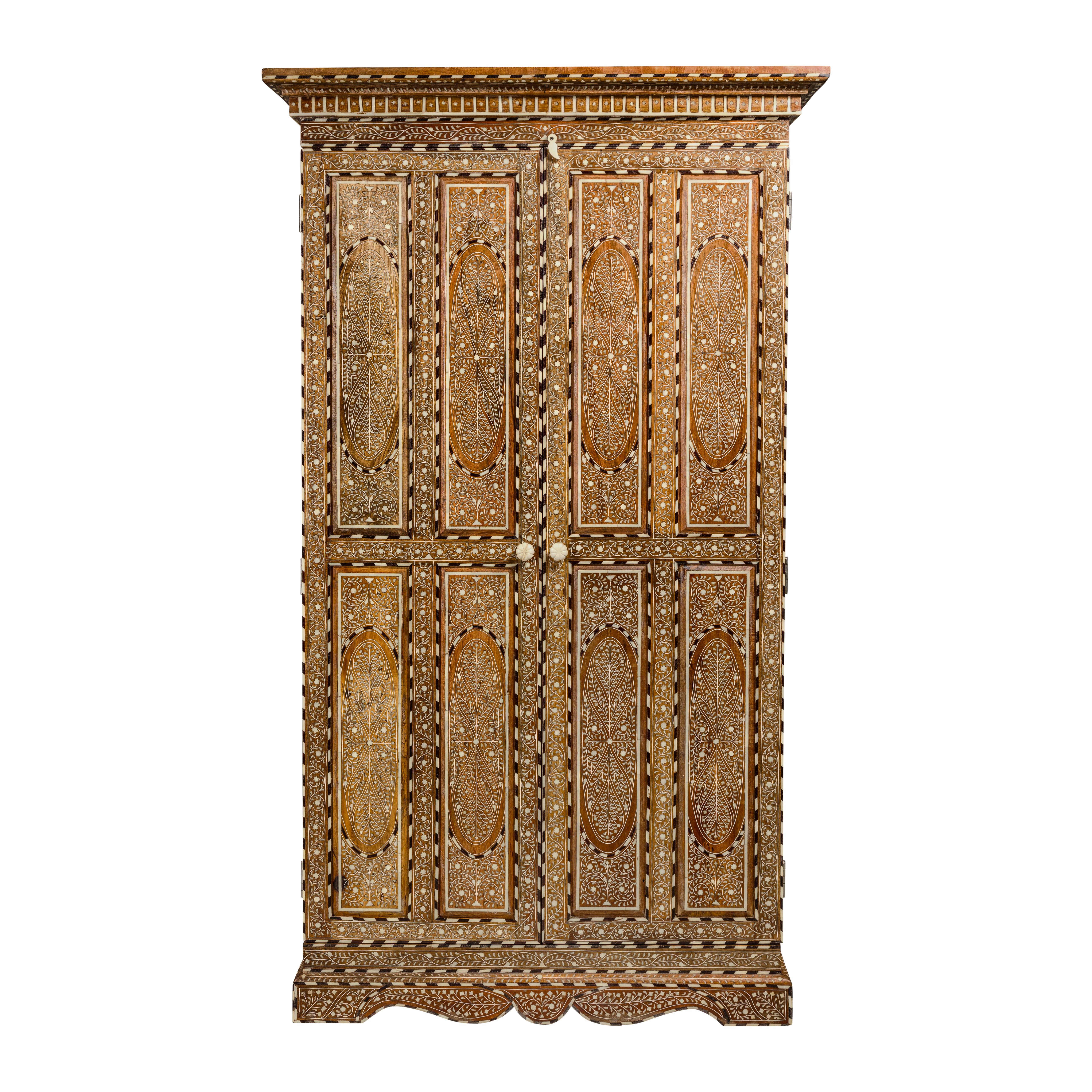 An Anglo-Indian style inlaid mango wood wardrobe cabinet from the mid-20th century, with floral themed bone inlay. This mid-20th-century Anglo-Indian style wardrobe cabinet is a true masterpiece of craftsmanship and design. Its enchanting presence