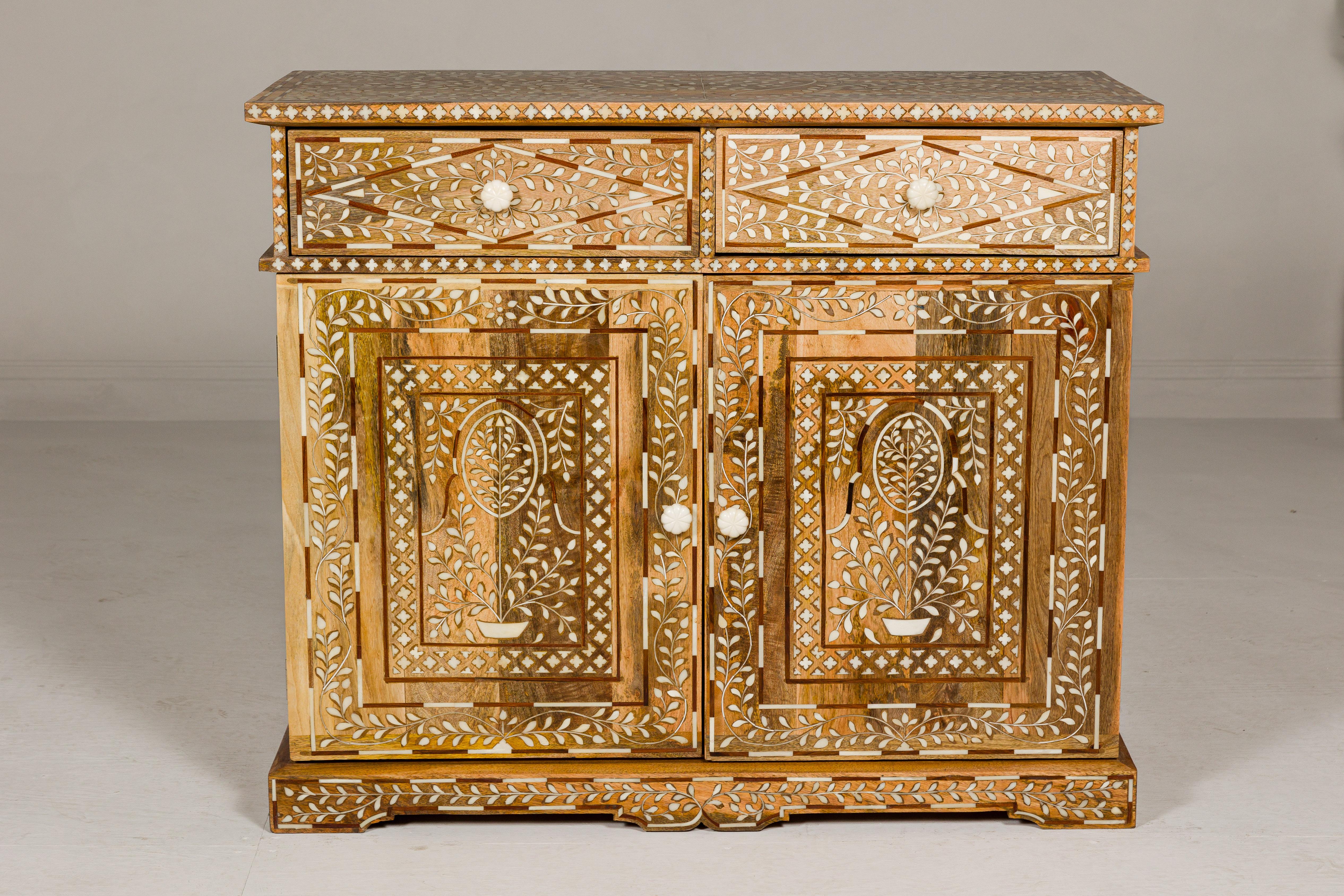 An Anglo-Indian style mango wood buffet with two drawers over two doors, lighter patina and bone hardware. This Anglo-Indian style mango wood buffet is a masterpiece of craftsmanship and design, exuding timeless elegance and artistic flair. With its