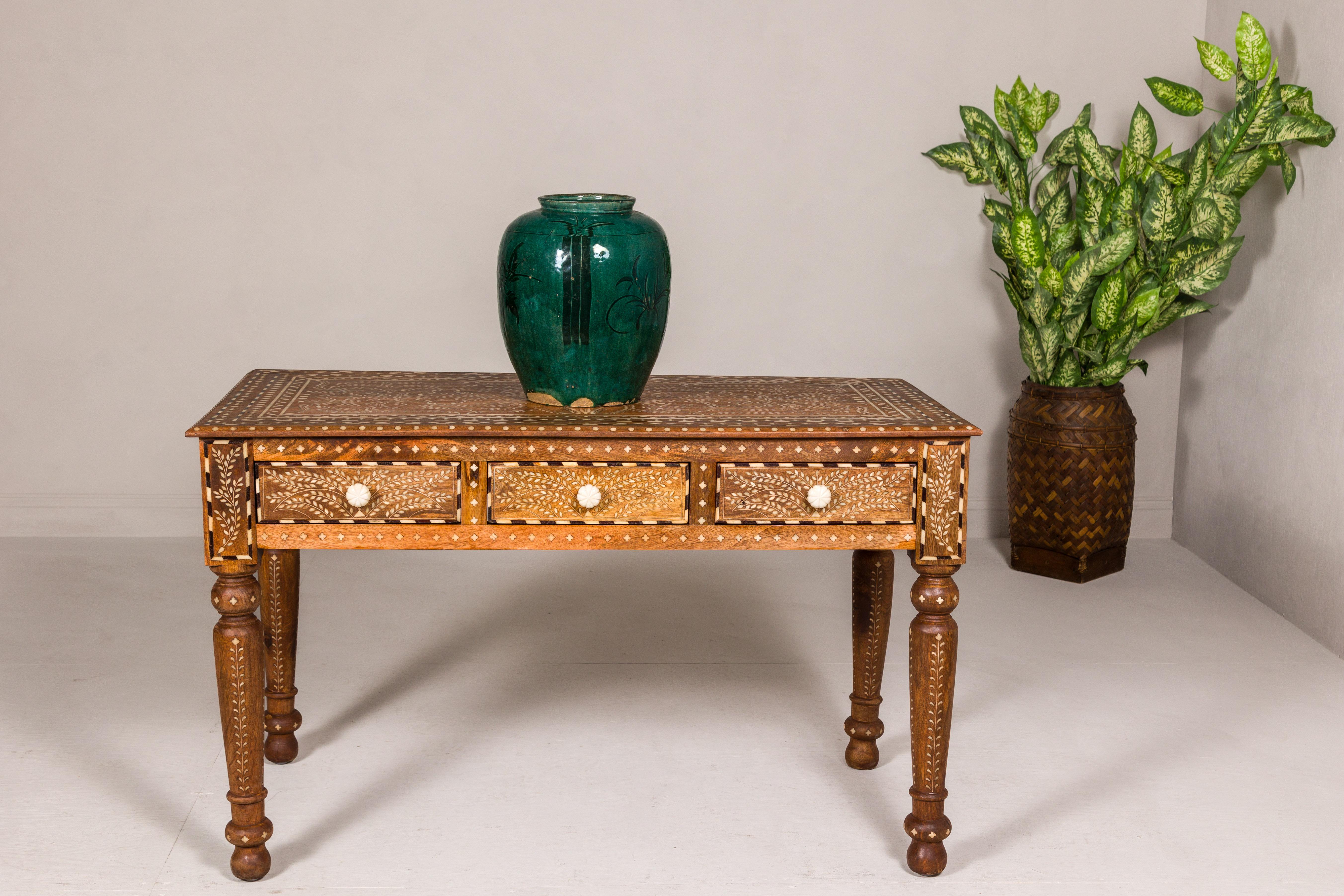 An Anglo-Indian style mango wood console table or desk with inlaid bone décor, three drawers and turned legs. Behold the ornate artistry of this Anglo-Indian style mango wood console table or desk, an epitome of craftsmanship that transcends