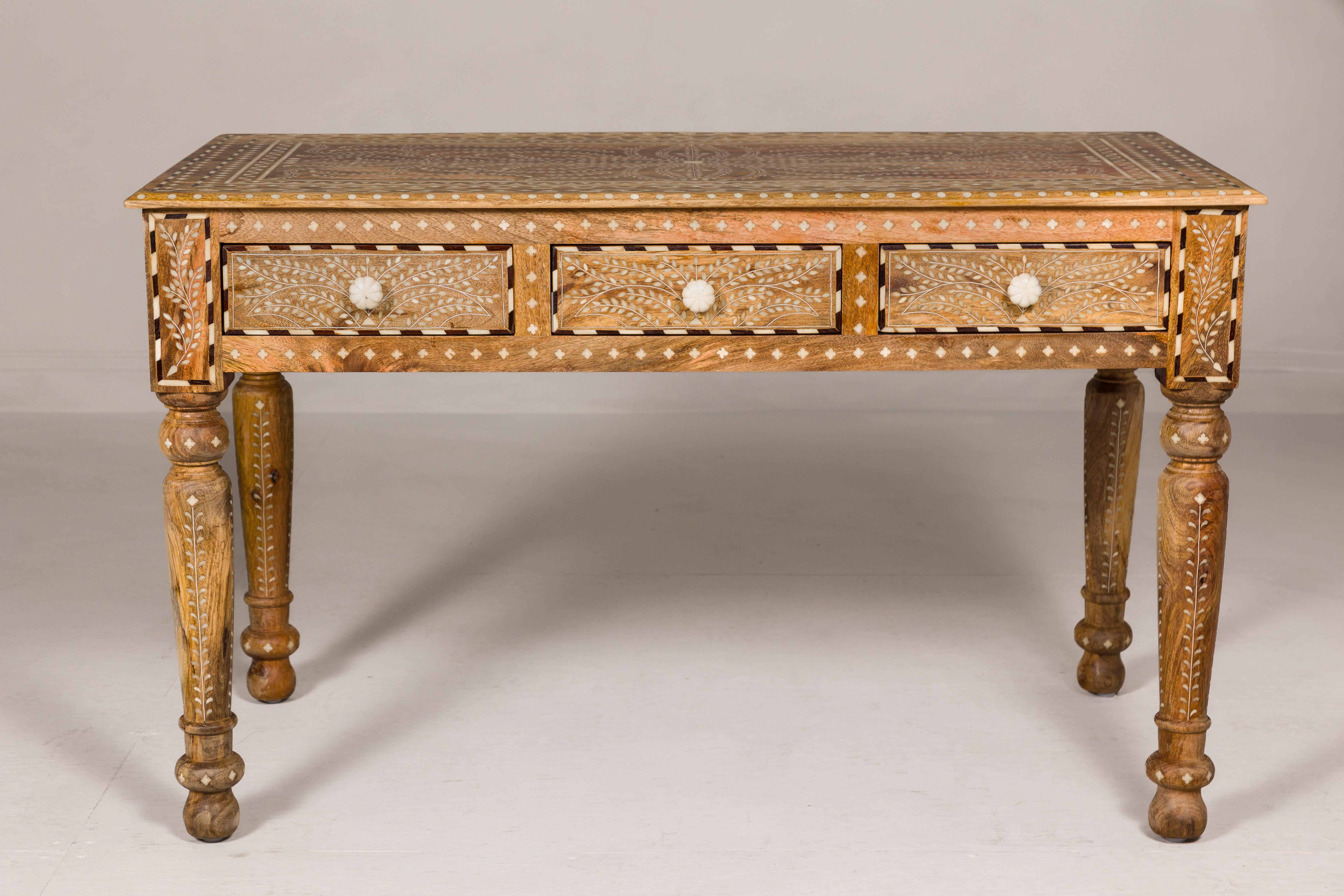An Anglo-Indian style mango wood console table or desk with inlaid bone décor, three drawers and turned legs. This Anglo-Indian style mango wood console table or desk is a true testament to the artistry of its makers. Its intricate bone inlay decor,