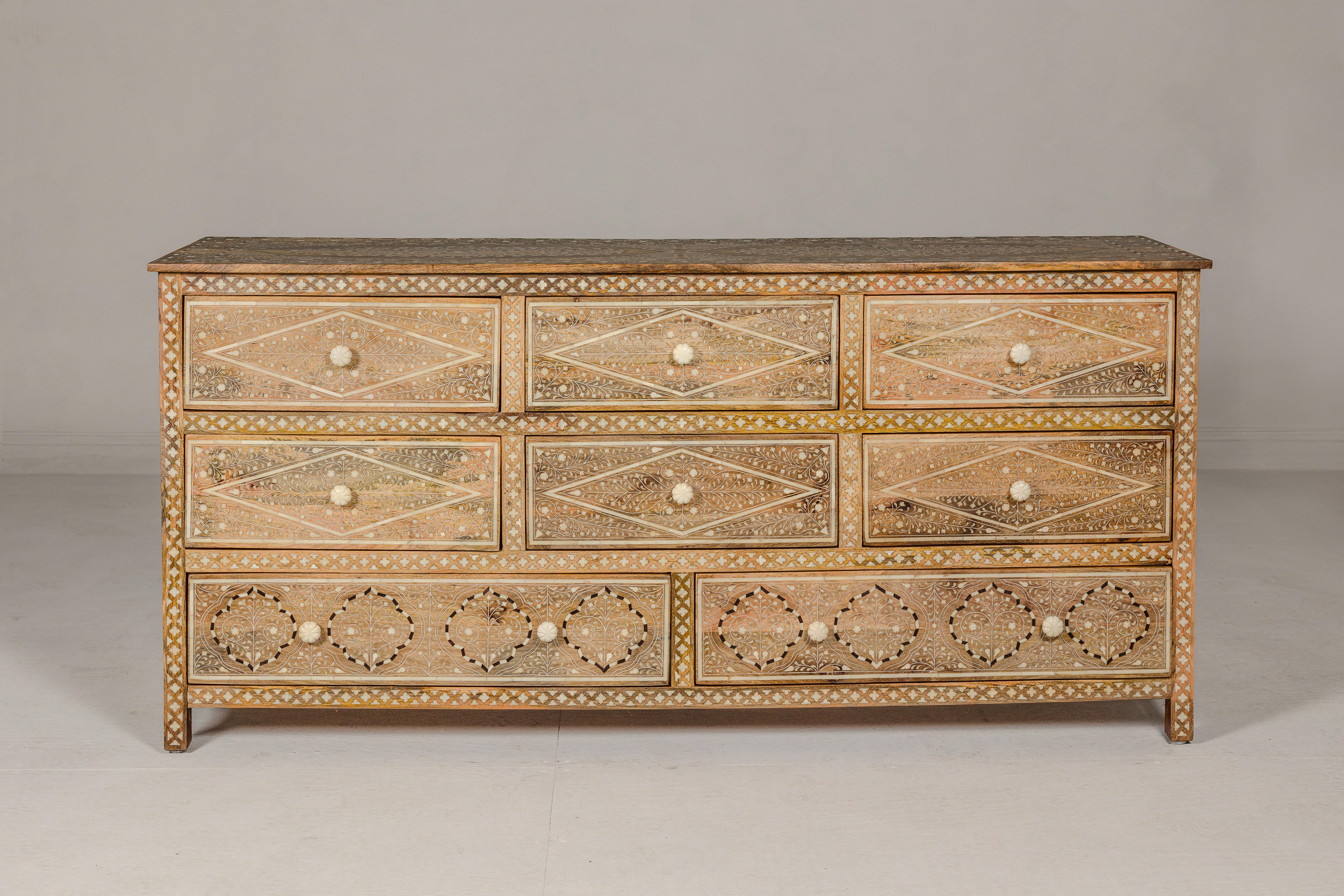 An Anglo-Indian style mango wood dresser with eight drawers, bone inlaid décor showcasing scrolling foliage and bone hardware. This exquisite Anglo-Indian style mango wood dresser is a testament to intricate craftsmanship and elegant design.