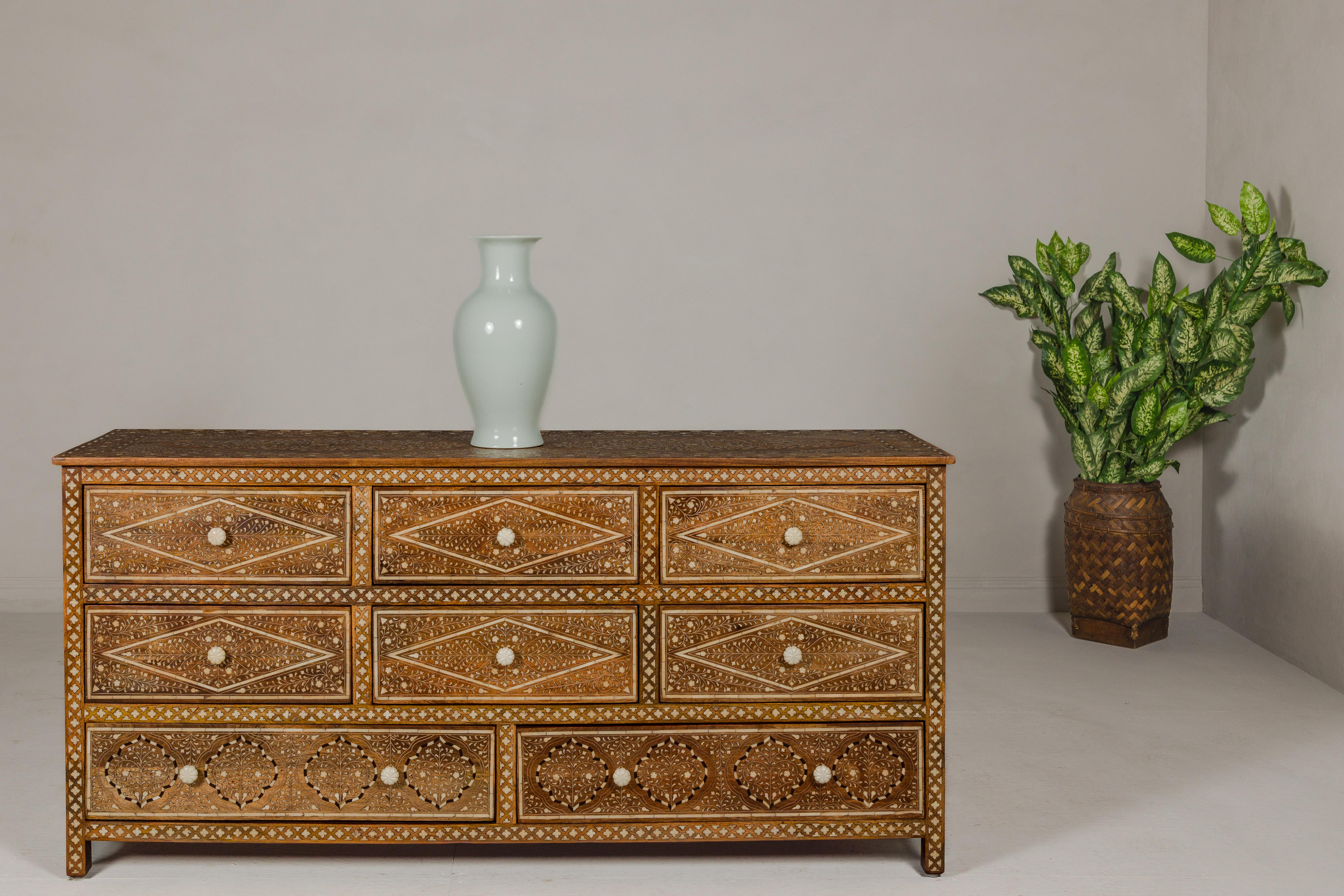 An Anglo-Indian style mango wood dresser with eight drawers, bone inlaid décor showcasing scrolling foliage and bone hardware. Gracefully composed, this Anglo-Indian style mango wood dresser merges the traditional charm of bone inlay with the robust