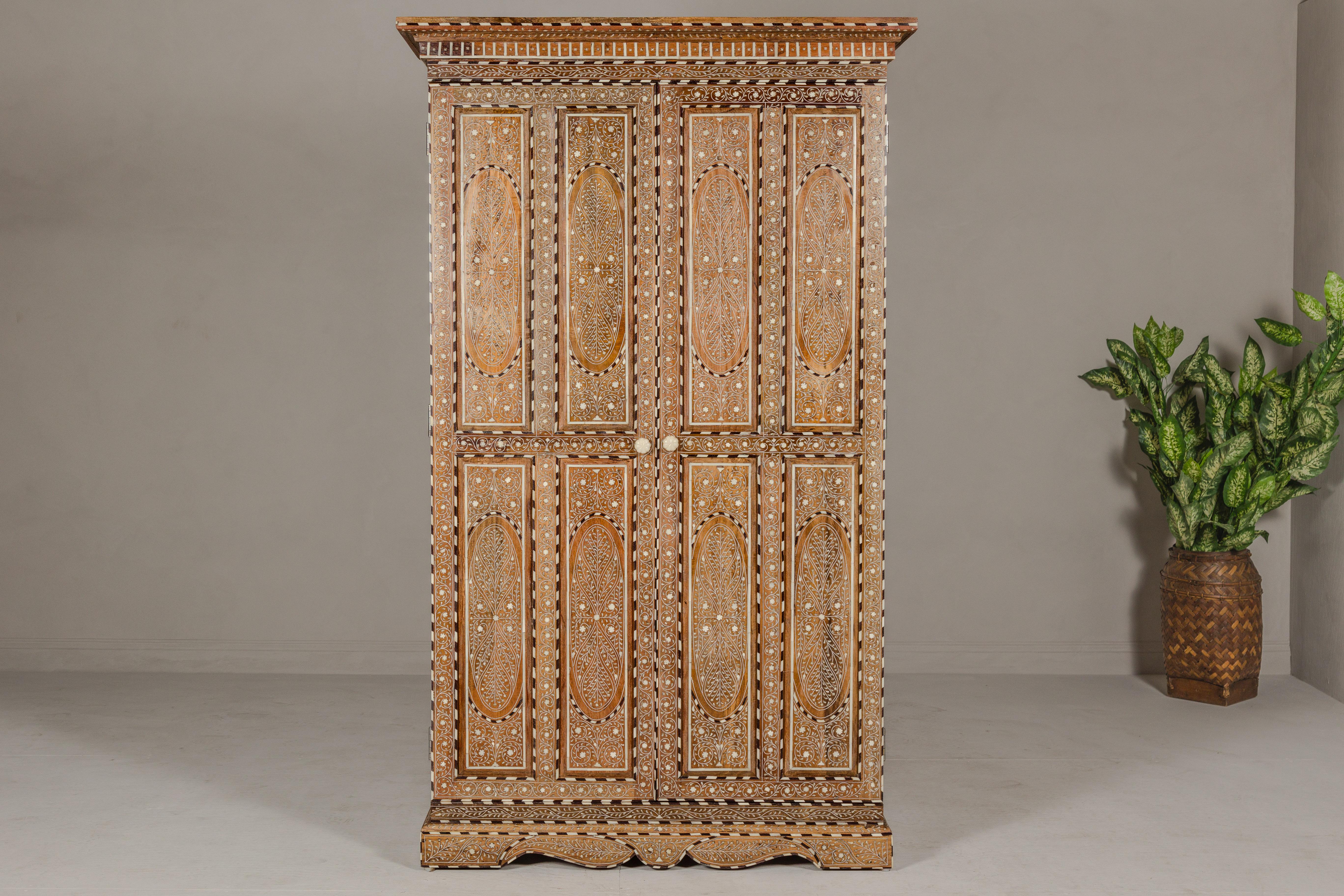 An Anglo-Indian style tall armoire made of mango wood and adorned with floral-themed bone inlay. Behold the magnificence of this Anglo-Indian style tall armoire, a true masterpiece crafted from the robust and warm-hued mango wood. Adorned with an