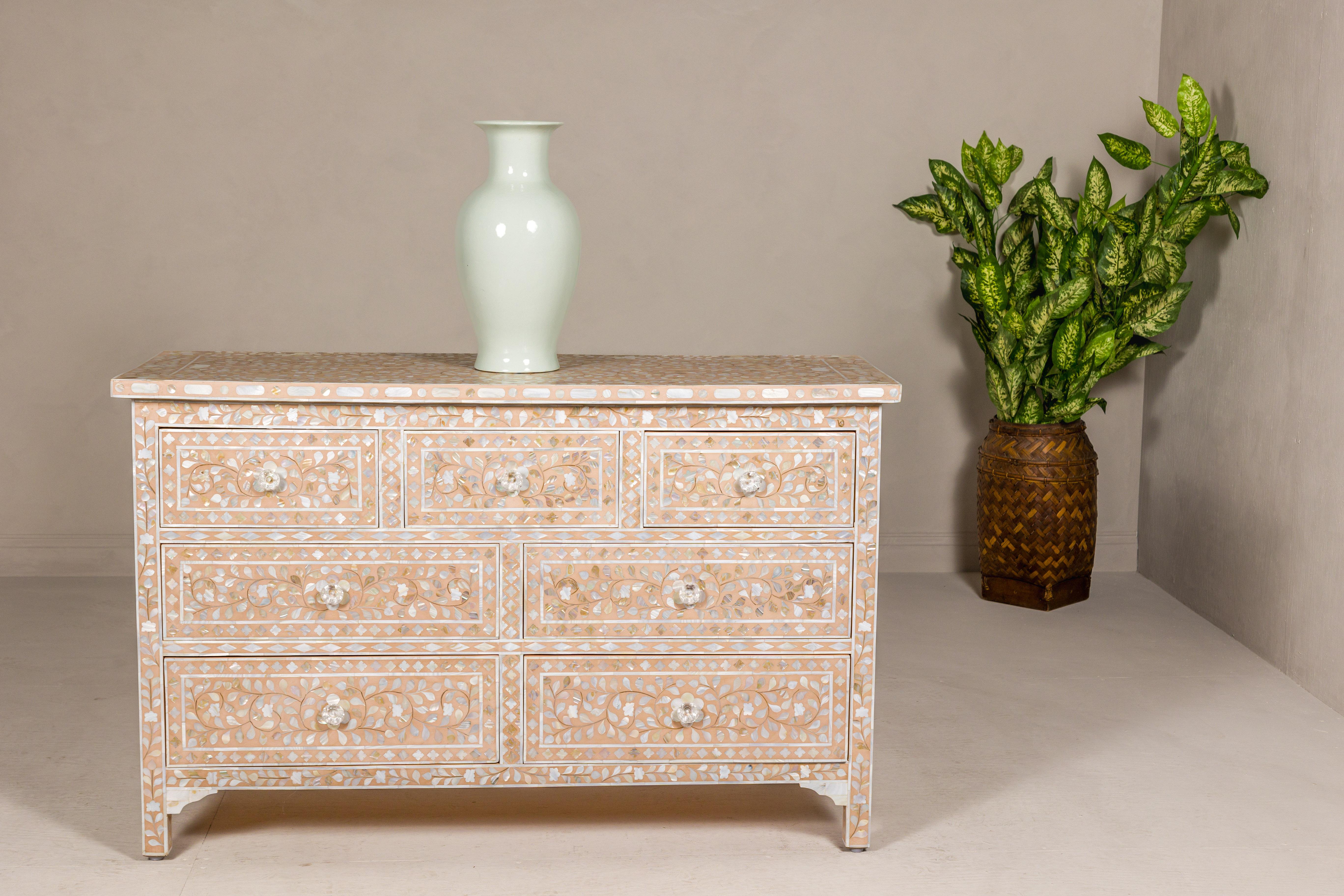 An Anglo-Indian style soft pink dresser with floral themed mother-of-pearl inlay and seven drawers. Radiating an air of refined elegance, this Anglo-Indian style dresser, bathed in a soft pink hue, is a true symphony of artistry and function.