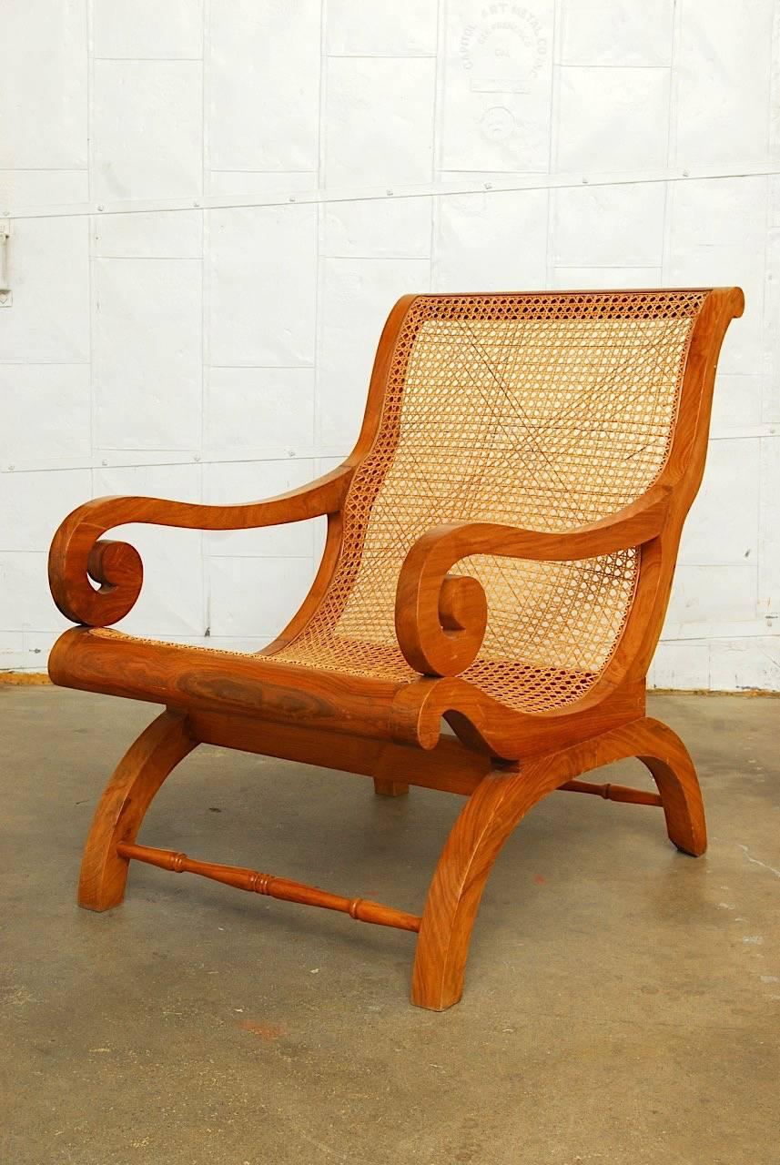 Hand-carved British Colonial plantation chair or planter's chair made of Anglo-Indian radiant grain teak and cane. Also known as a Campeche chair. The chair has large Regency style scrolled arms and an X-form frame. Graceful and comfortable with
