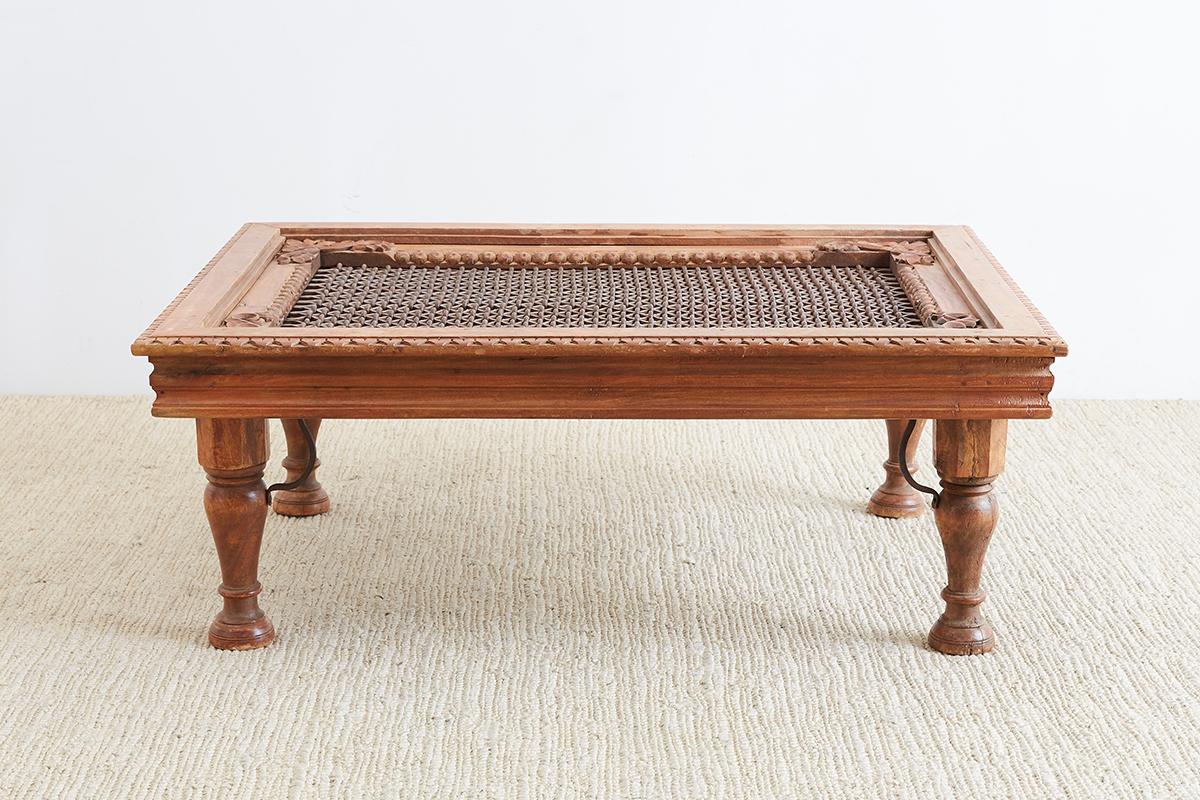 Fantastic Anglo-Indian hand-carved teak window made in to a coffee table. Features a geometric lattice window grill with a thick iron open fretwork design. The frame has intricately carved scrolls and decorative border designs. Supported by thick,