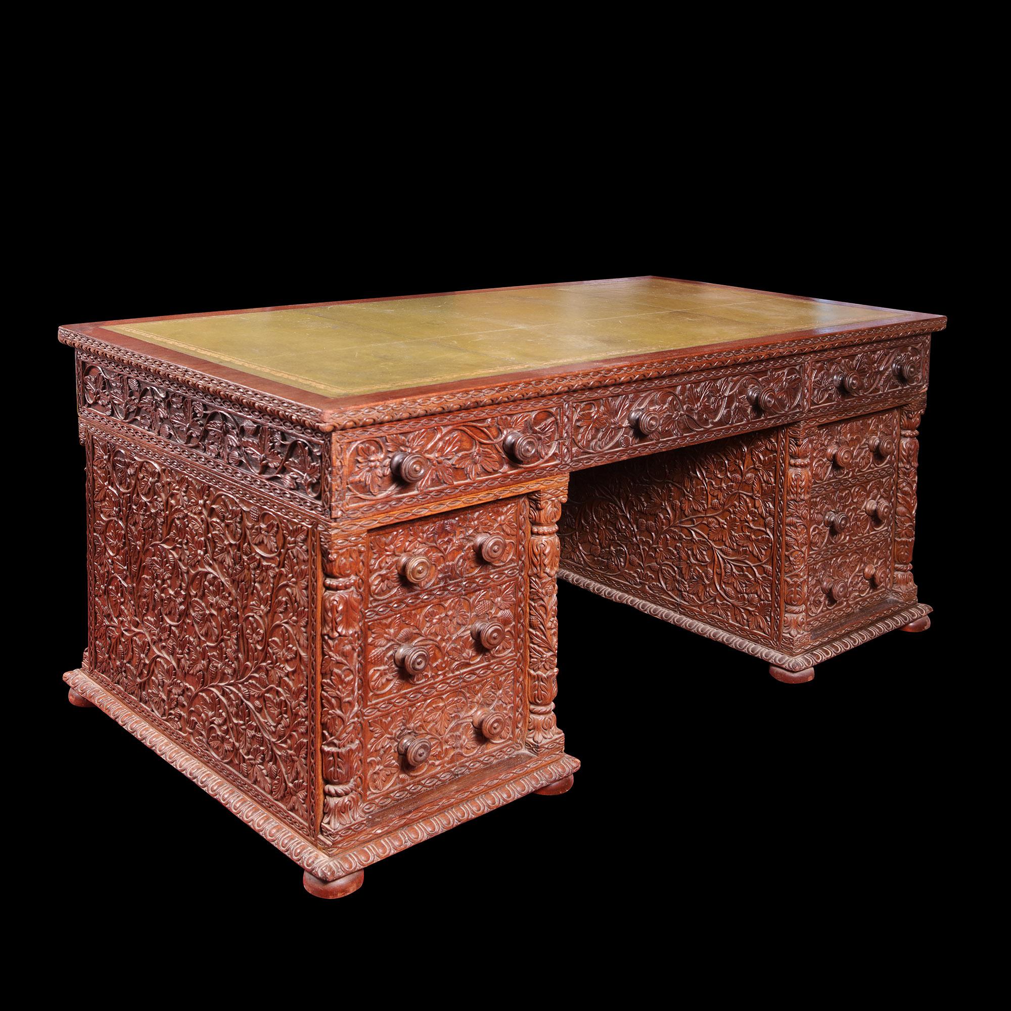 A late 19th century Anglo Indian Pedestal desk, profusely decorated with scrolling vines with abundant leaves and fruit. The desk carved on all sides, with two banks of three drawers in the pedestals and three short drawers along the frieze. Now