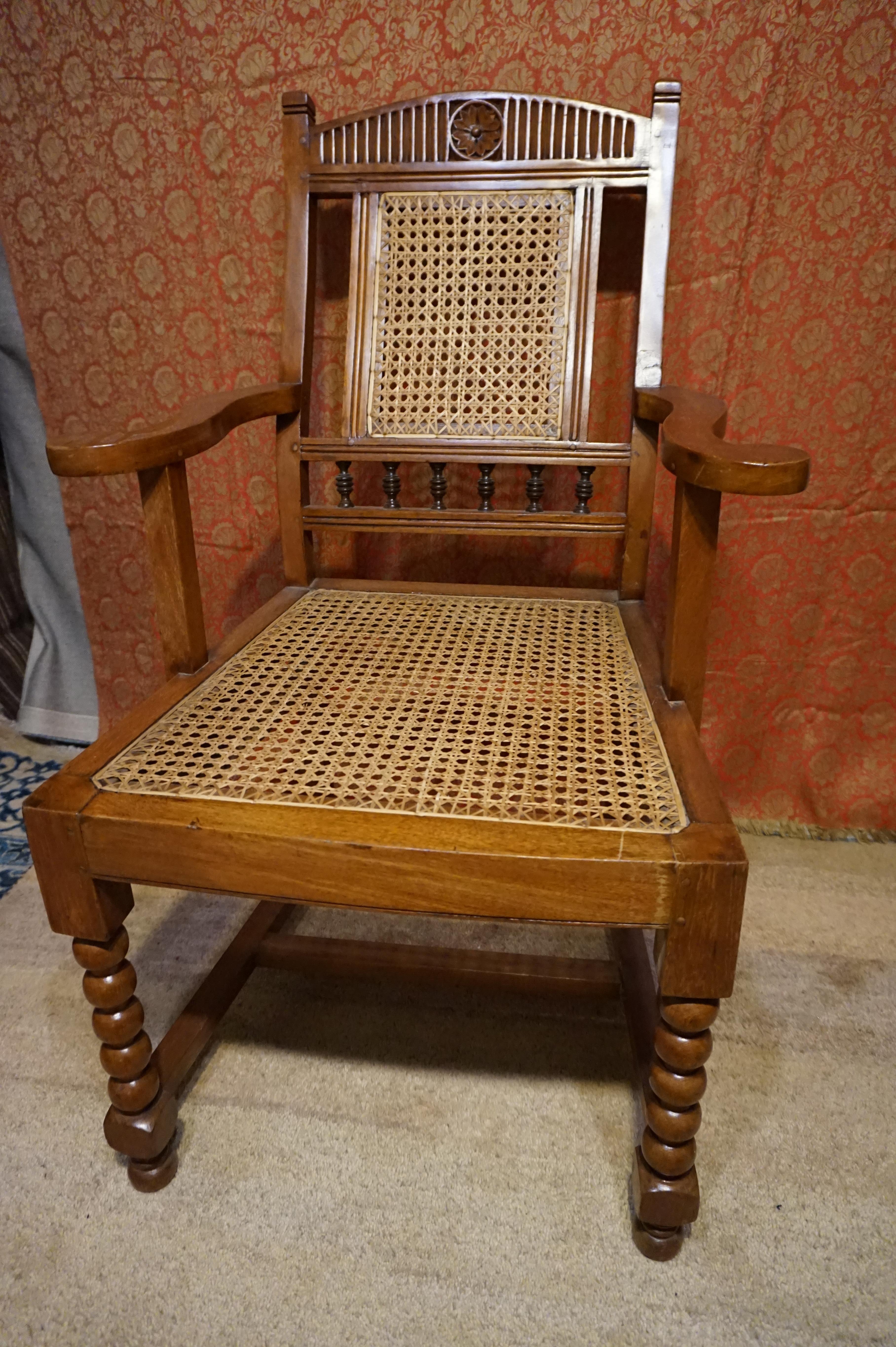 Beautifully hand carved teak armchair likely constructed for the British in India. Several elements that make it unique including scrolling arms, barley twist legs, reclining back, carved backrest, cane work etc. Wonderful patina. Sturdy but one leg