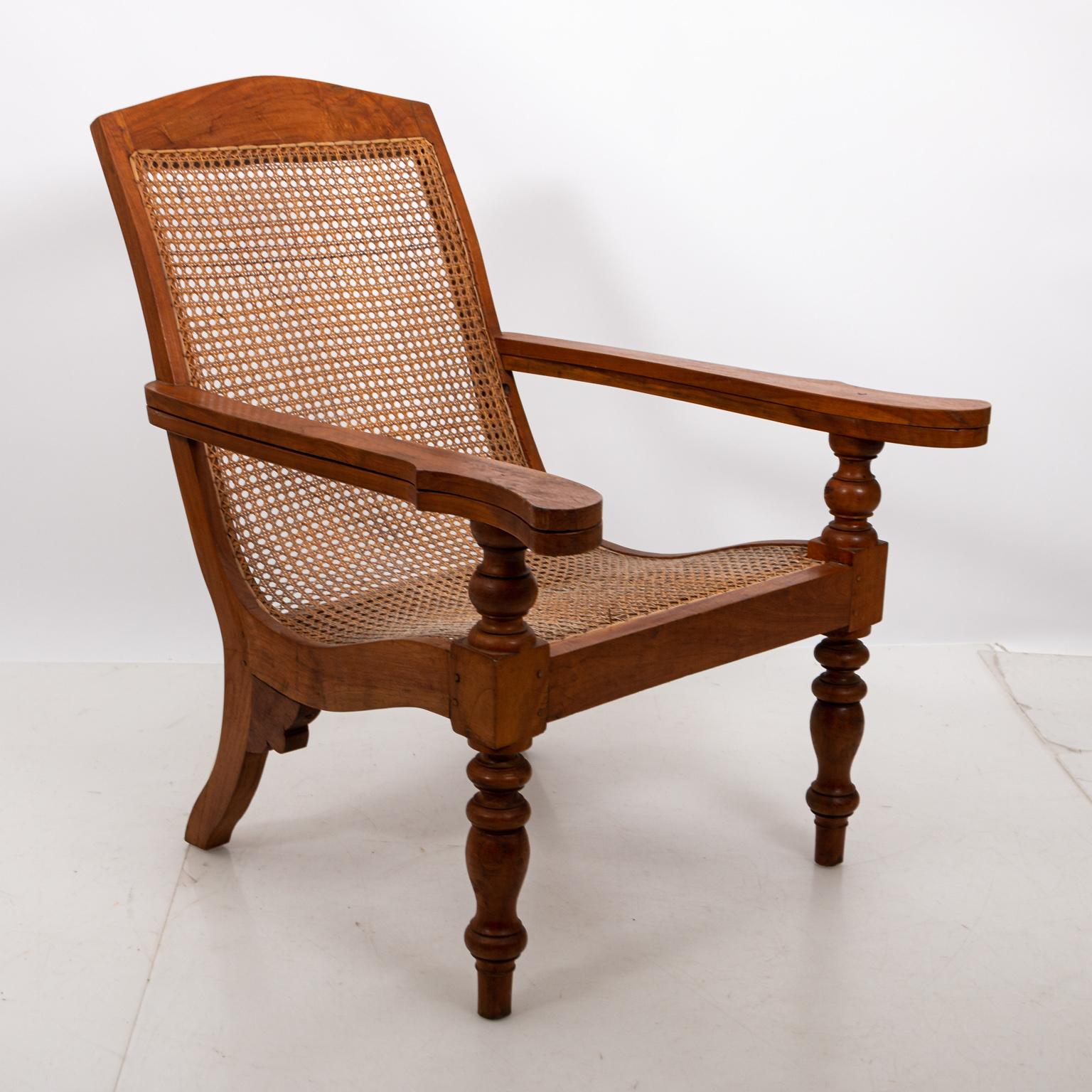 Anglo-Indian plantation chair in Teak with cane woven seat and back. The piece also features extendable armrests on turned legs. Please note of wear consistent with age including minor finish loss to the wood and cane. Made in India, circa