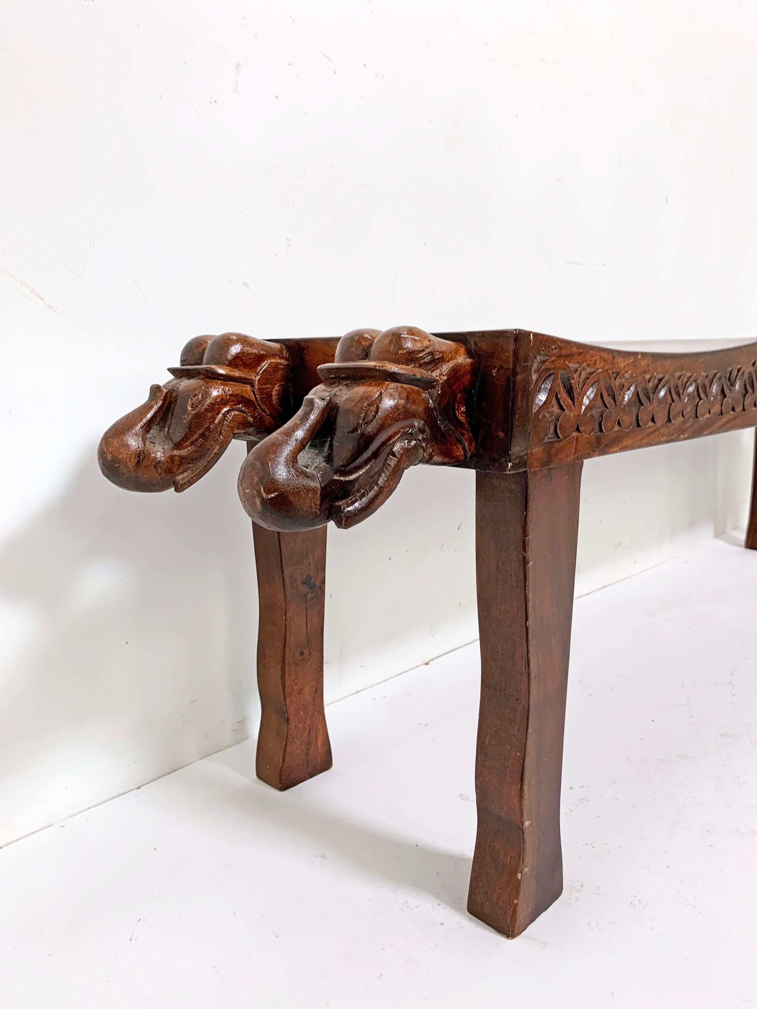 A sculpturally whimsical Anglo-Indian three-seat bench with decorative elephant head carvings at either end, circa 1970s.