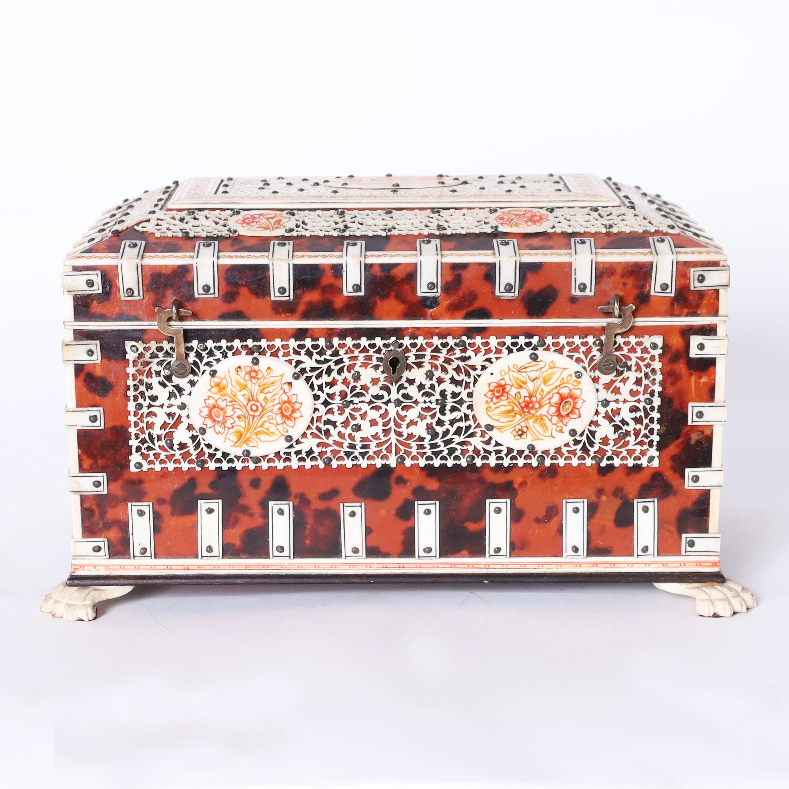 Impressive Anglo Indian box crafted in mahogany and clad in tortoise shell decorated with bone straps, carved and painted floral panels, and paw feet. The inside has a mirror and bone decorated removable compartments.