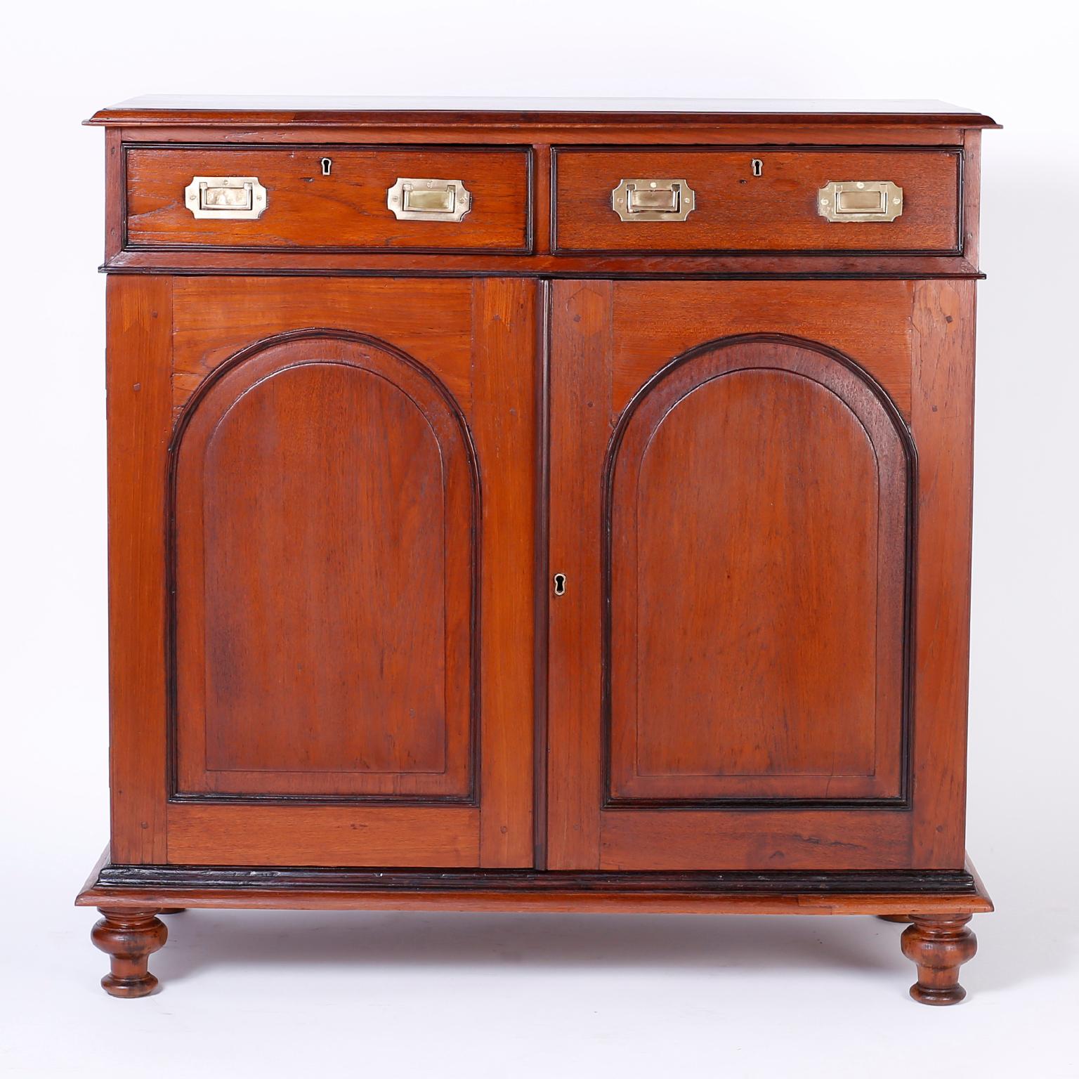 Antique Anglo-Indian mahogany cabinet or buffet with two drawers over two doors with beveled arch cutout. Featuring hand pegged construction, brass Campaign hardware, ebonized trim, and turned feet.
 