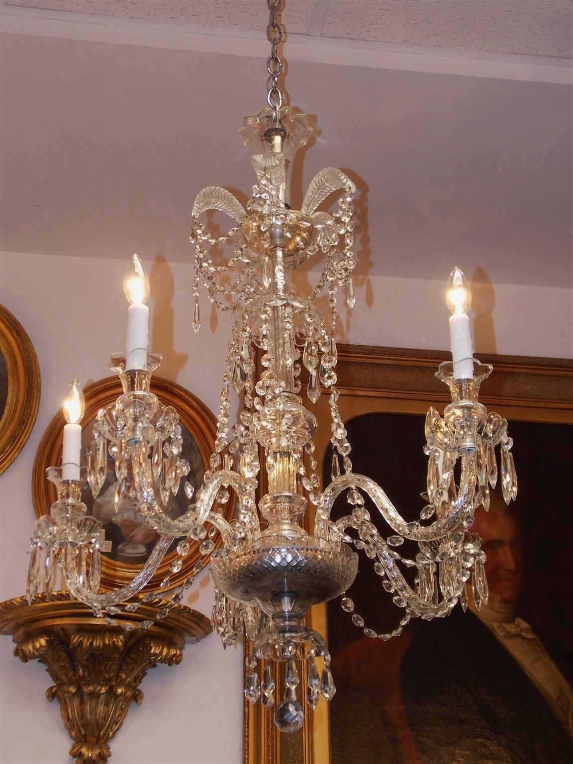Anglo-irischer fünfarmiger Kronleuchter aus geschliffenem Kristall mit Federschmuck, zentraler bauchiger Säule, kaskadenförmigen Prismen und einer geschliffenen Kristallschale mit facettierter Kugel. Mitte des 19. Jahrhunderts. Der Kronleuchter war