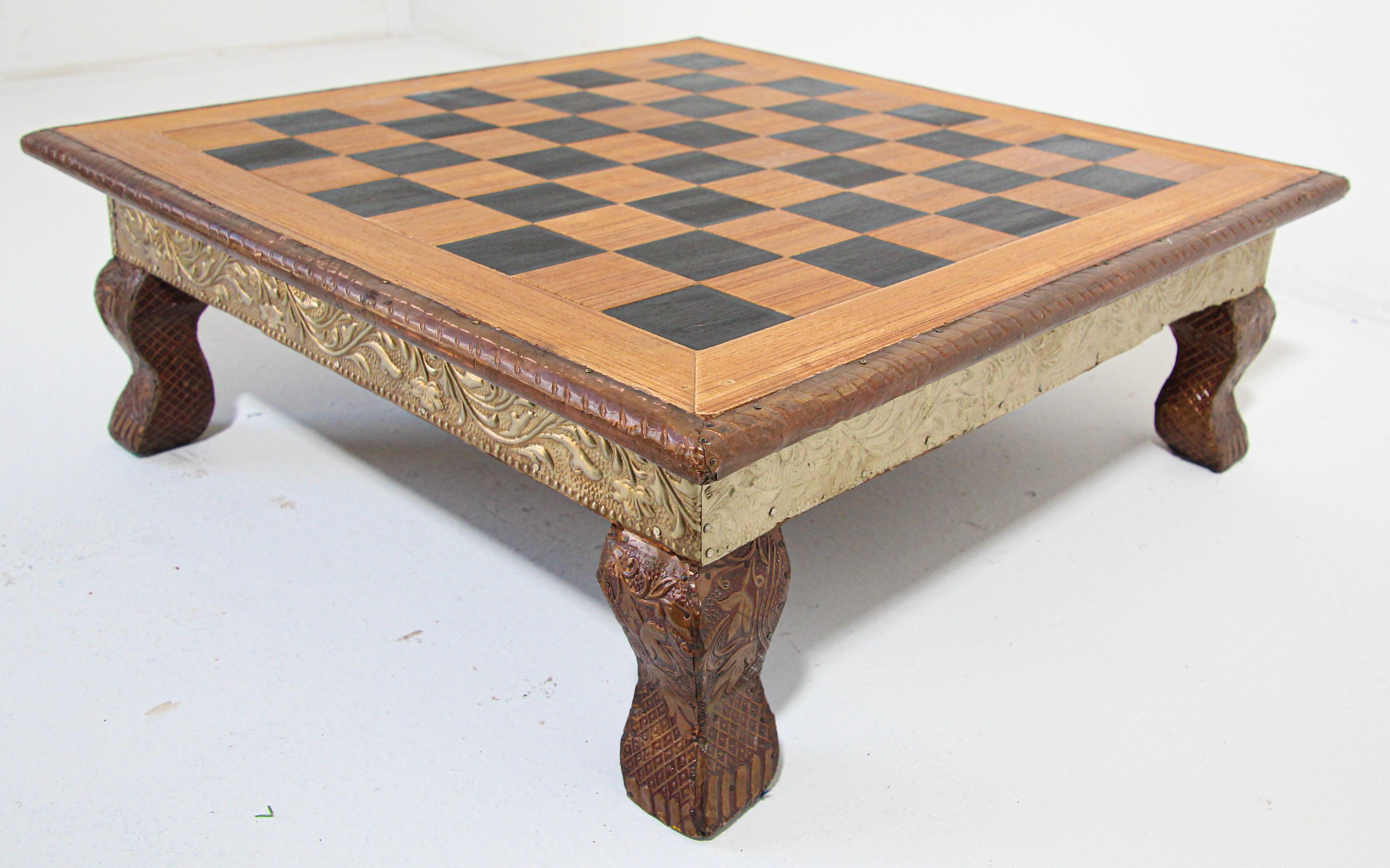 The board is nicely carved with Rajasthani designs at the rim, the sides and feet are covered with clad silver metal hammered with Moorish Raj designs. 
In good vintage condition. 
Wood table with board size 7 inches tall, 20 inches square framed,