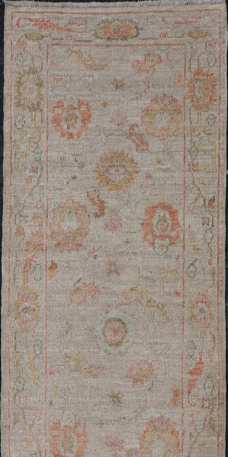This angora Oushak is unique with is creamy background, to the floral like design rendered in coral, tangerine, forest green, salmon, and hints of sky blue. The border is harmonious in design and color, giving the piece a light and elegant yet