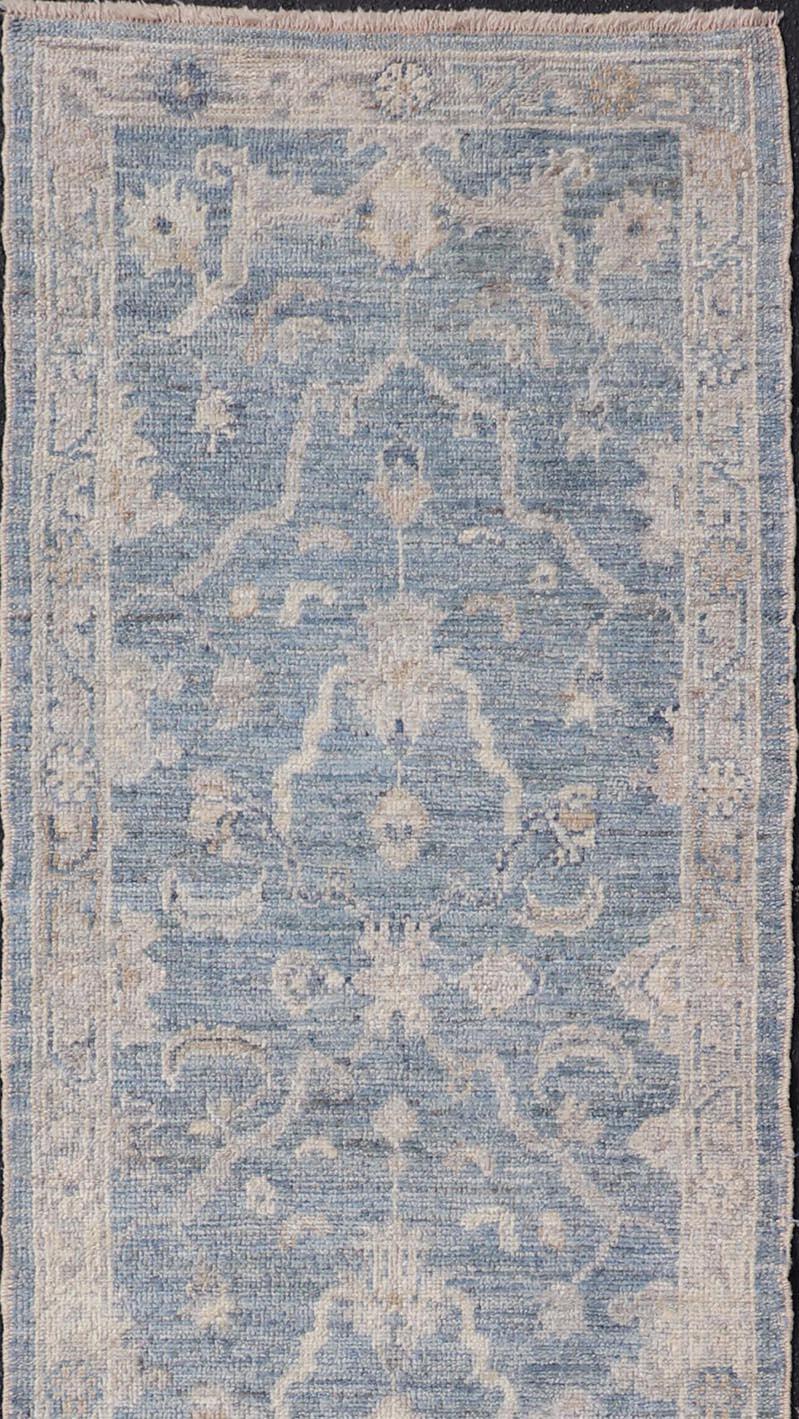 This Oushak Runner is rendered in a medium blue background and a light gray border. The design is an arabesque-like floral pattern, cased within a banded sub-floral border in light gray. 

Measures; 2'6 x 10'6 

Angora Turkish Oushak Runner with