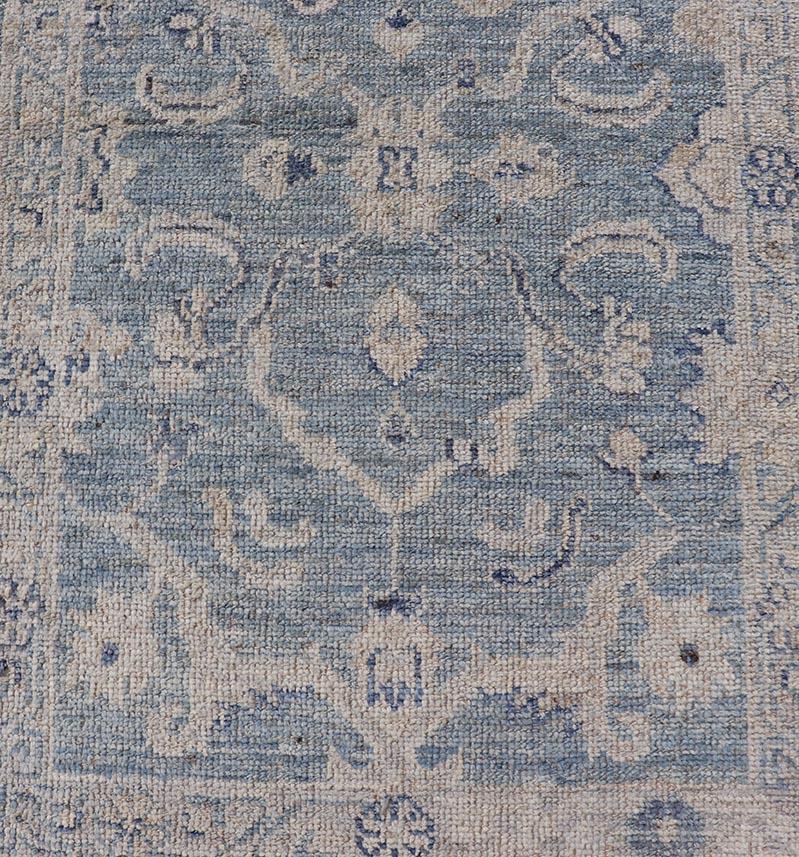 This Oushak Runner is rendered in a medium blue background and a light grey border. The design is an arabesque-like floral pattern, cased within a banded sub-floral border in light grey. 
Measures: 2'7 x 11'8 

Angora Turkish oushak runner with