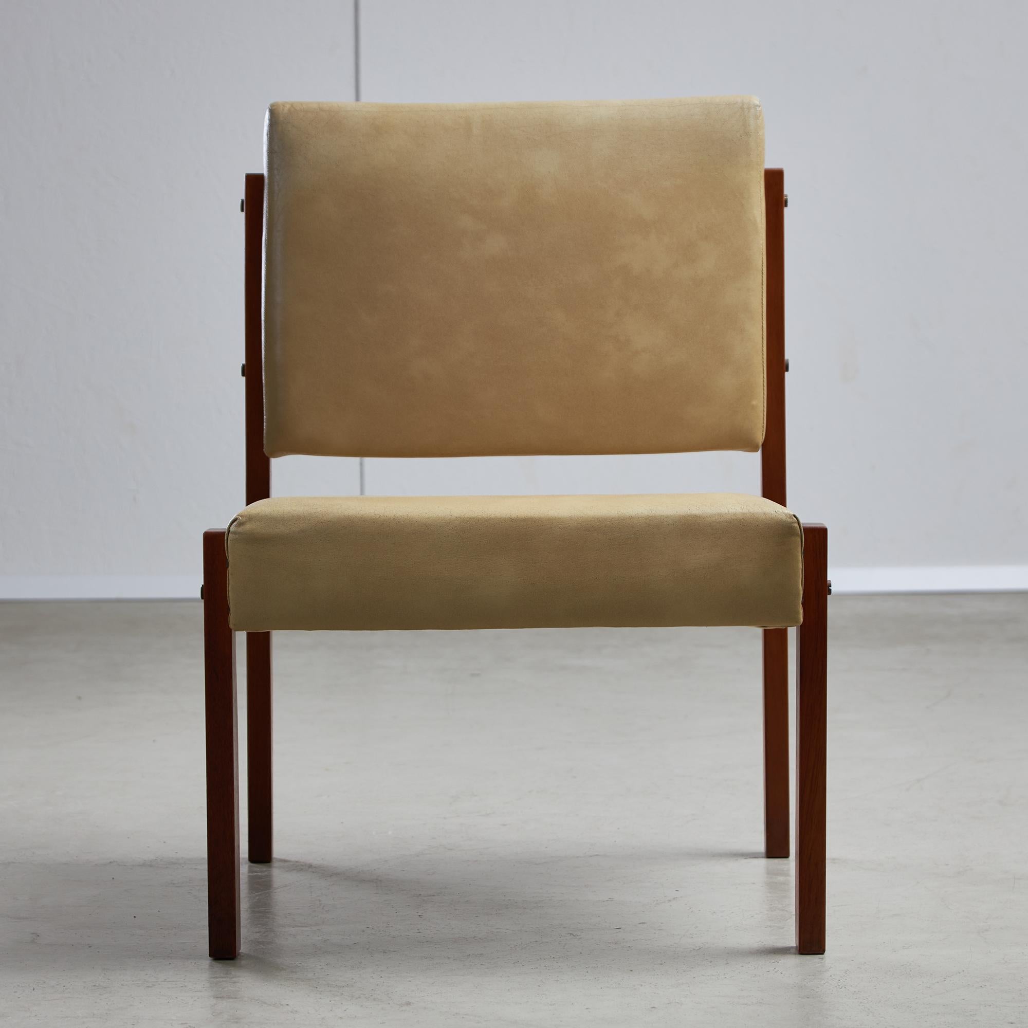 Una silla baja y angulosa de madera de teca de los años 70. Fabricada con tornillos de cobre y tapizada en suave piel beige, esta silla presenta líneas afiladas y detalles distintivos que realzan cualquier espacio. El diseño incorpora un asiento