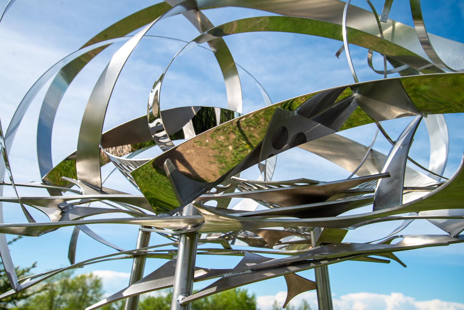 In this elegant sculpture by Ania Biczysko, fine ribbons of stainless-steel overlap in circles forming a cloud-like structure mounted on a tripod stand. When viewed from all sides, the sky is reflected in the luminescent quality of the polished