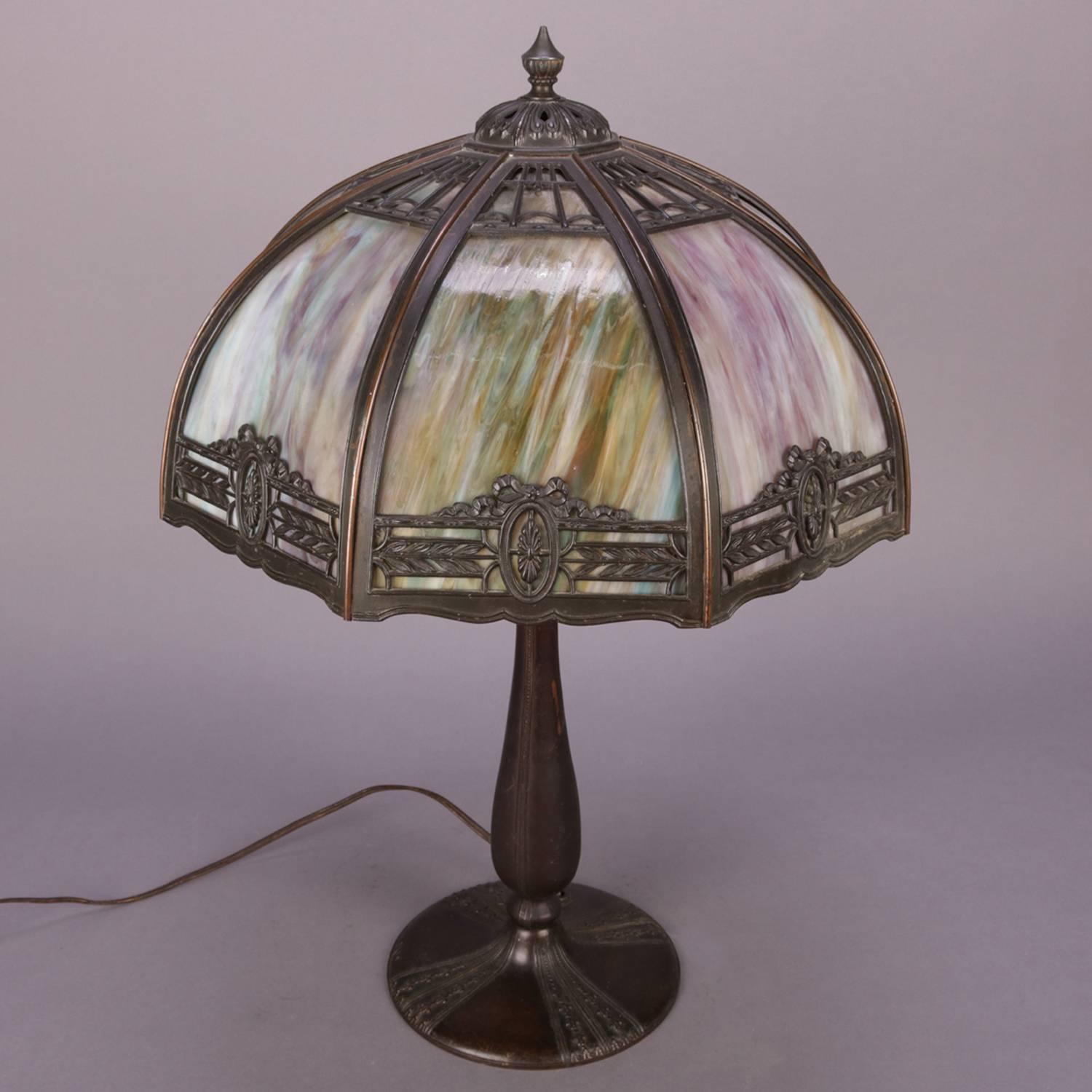 Antique Bradley & Hubbard School table lamp features eight panel pierced filigree shade with foliate border containing patera medallions central to each panel and housing curved slag glass panes, cast base is tulip form with dual pull chain light