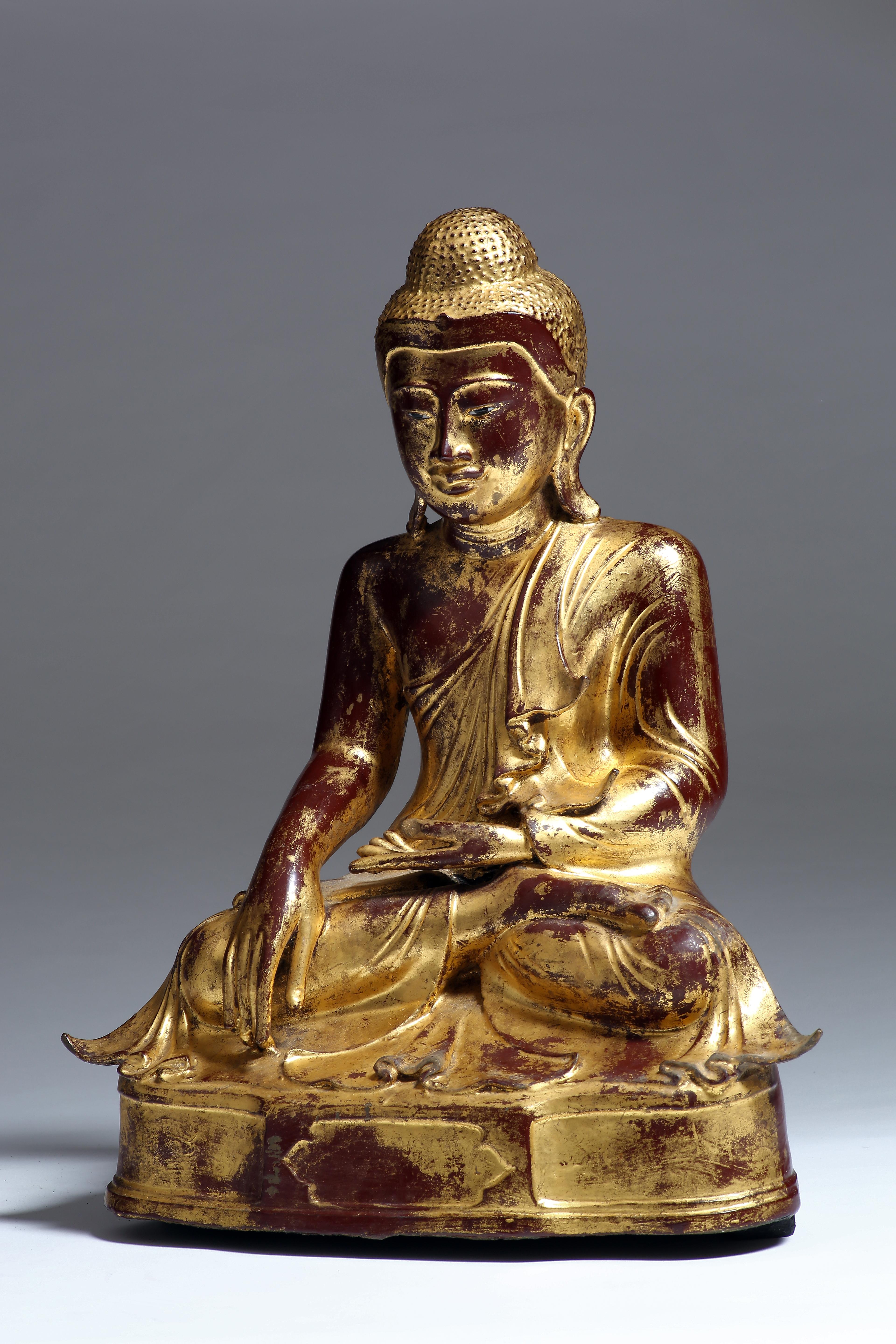 The Buddha is seated on a low base in vajrasana (lotus) position with bhumisparsha mudra, in which the finger-tips of the right hand touch the earth to symbolize the moment of enlightenment. The Buddha has a serene expression and is clothed in
