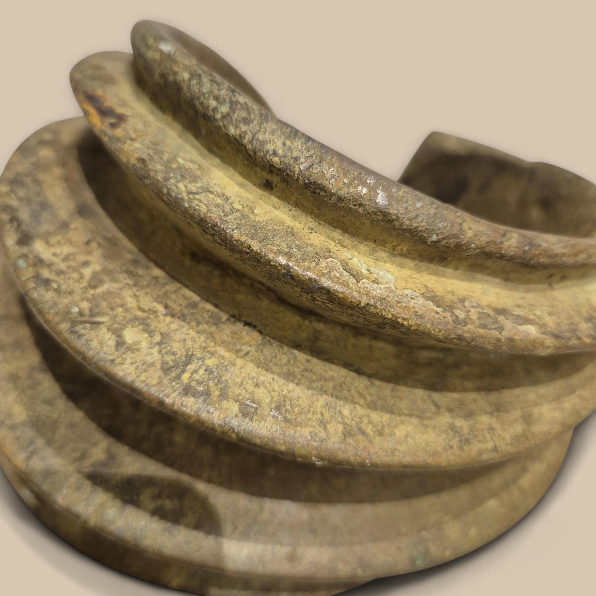 Beeindruckendes offenes Knöchelarmband aus einer Bronzelegierung mit einem breiten Ring, der mit sechs erhabenen Formen verziert ist. Die oxidierte, körnige Patina zeugt von seinem Alter und seiner rituellen Verwendung.

Diese oft schweren und