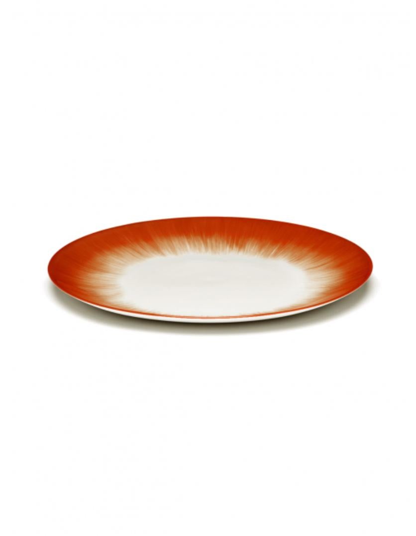 A set of two hand-painted porcelain Ann Demeulemeester 24 centimeter plates in off-white and red. A red matte glaze on the outside with a glossy off-white glaze on the inside. The contrast between matte and glossy, and the contrast between red and