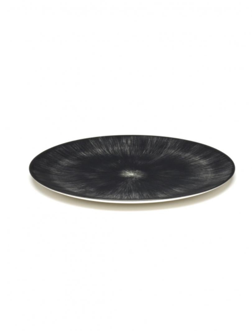 Set of two Ann Demeulemeester hand-painted porcelain 24 centimeter plates. A black matte glaze on the outside with a glossy off-white glaze on the inside. The contrast between matte and glossy, but also the contrast between black and off-white, are