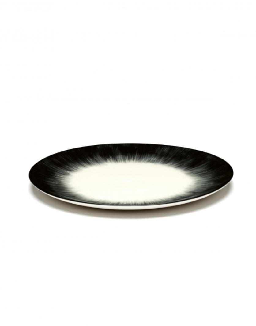 Juego de dos platos de porcelana pintada a mano Ann Demeulemeester de 24 centímetros. Un esmalte negro mate en el exterior con un esmalte brillante blanquecino en el interior. El contraste entre mate y brillante, pero también entre negro y blanco