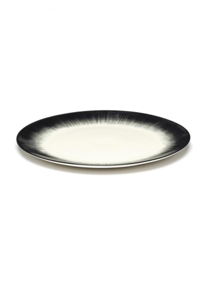 A set of two Ann Demeulemeester porcelain hand-painted 24 centimeter plates. A black matte glaze on the outside with a glossy off-white glaze on the inside. The contrast between matte and glossy, but also the contrast between black and off-white,