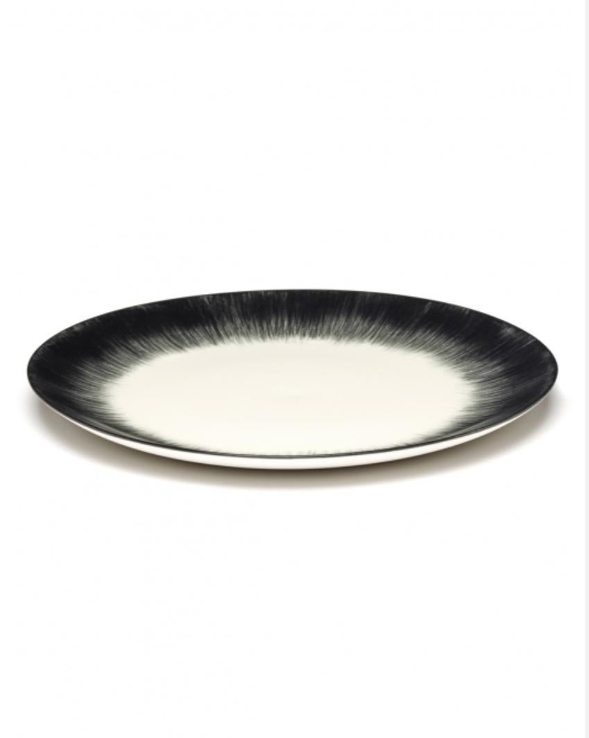A set of two 28 centimeter hand-painted porcelain plates from Ann Demeulemeester. A black matte glaze on the outside with a glossy off-white glaze on the inside. The contrast between matte and glossy, but also the contrast between black and
