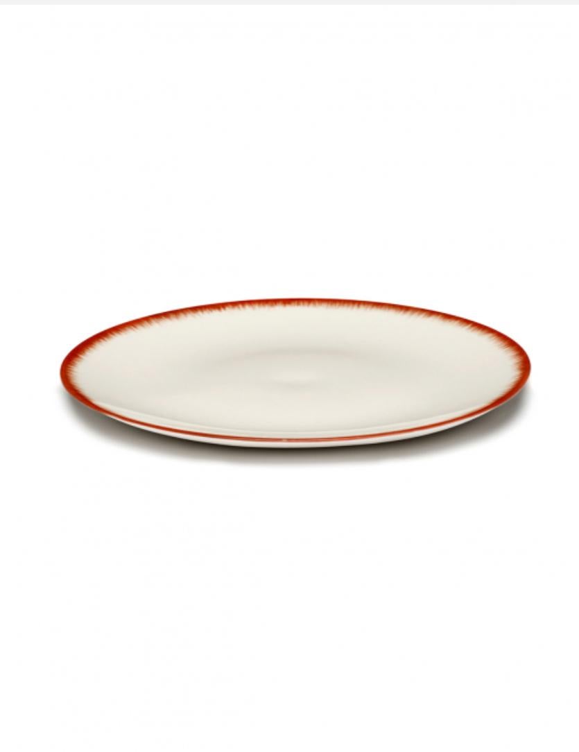 A set of two 28 centimeter hand-painted, porcelain plates from Ann Demeulemeester. A red matte glaze on the outside with a glossy off-white glaze on the inside. The contrast between matte and glossy, and the contrast between red and off-white, are
