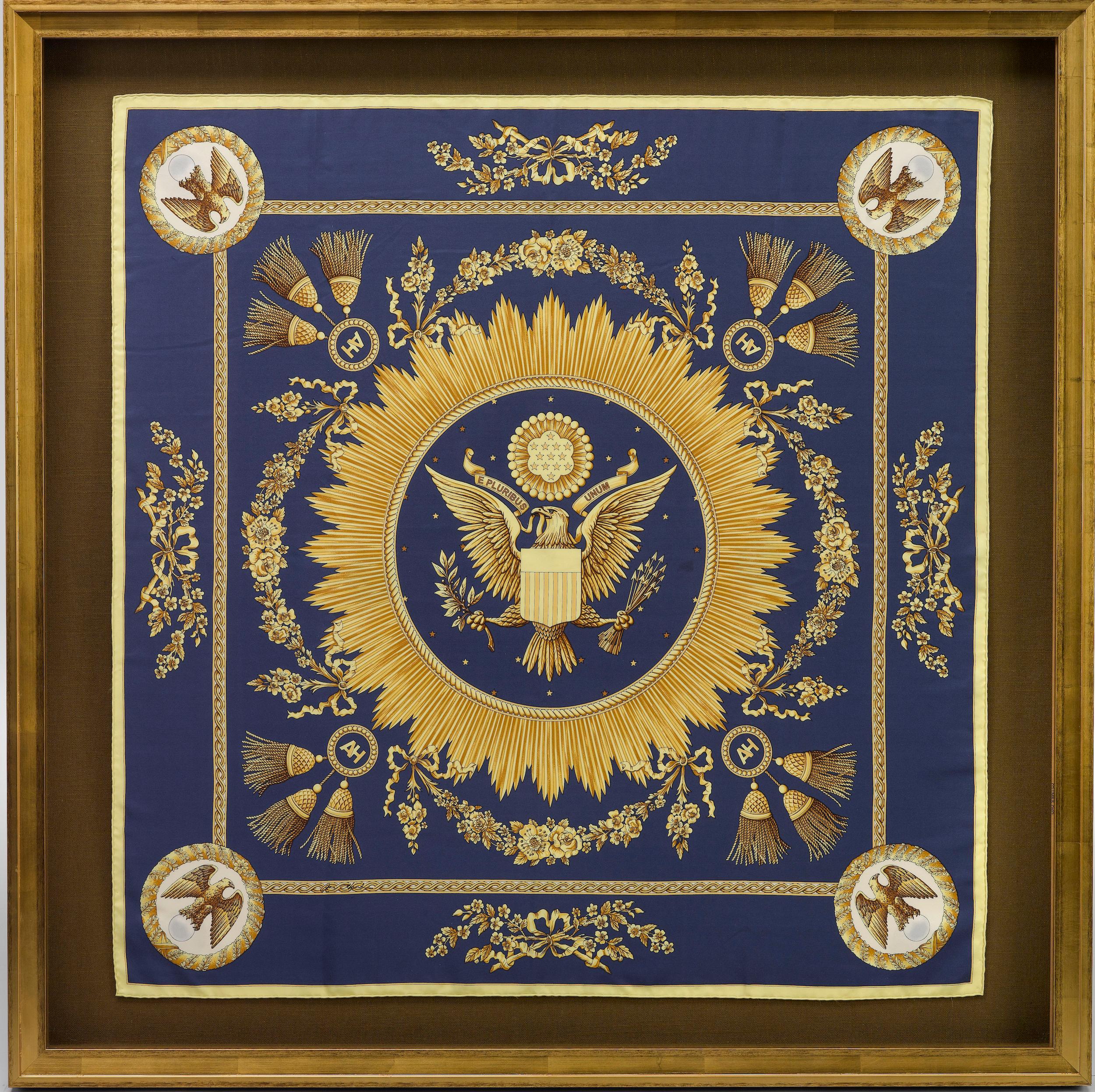This is a coveted, patriotic silk scarf, issued by American designer Ann Hand. The silk scarf was issued in a deep navy and gold colorway. At center is an artistic interpretation of the Great Seal of the United States. The Great Seal is set in a