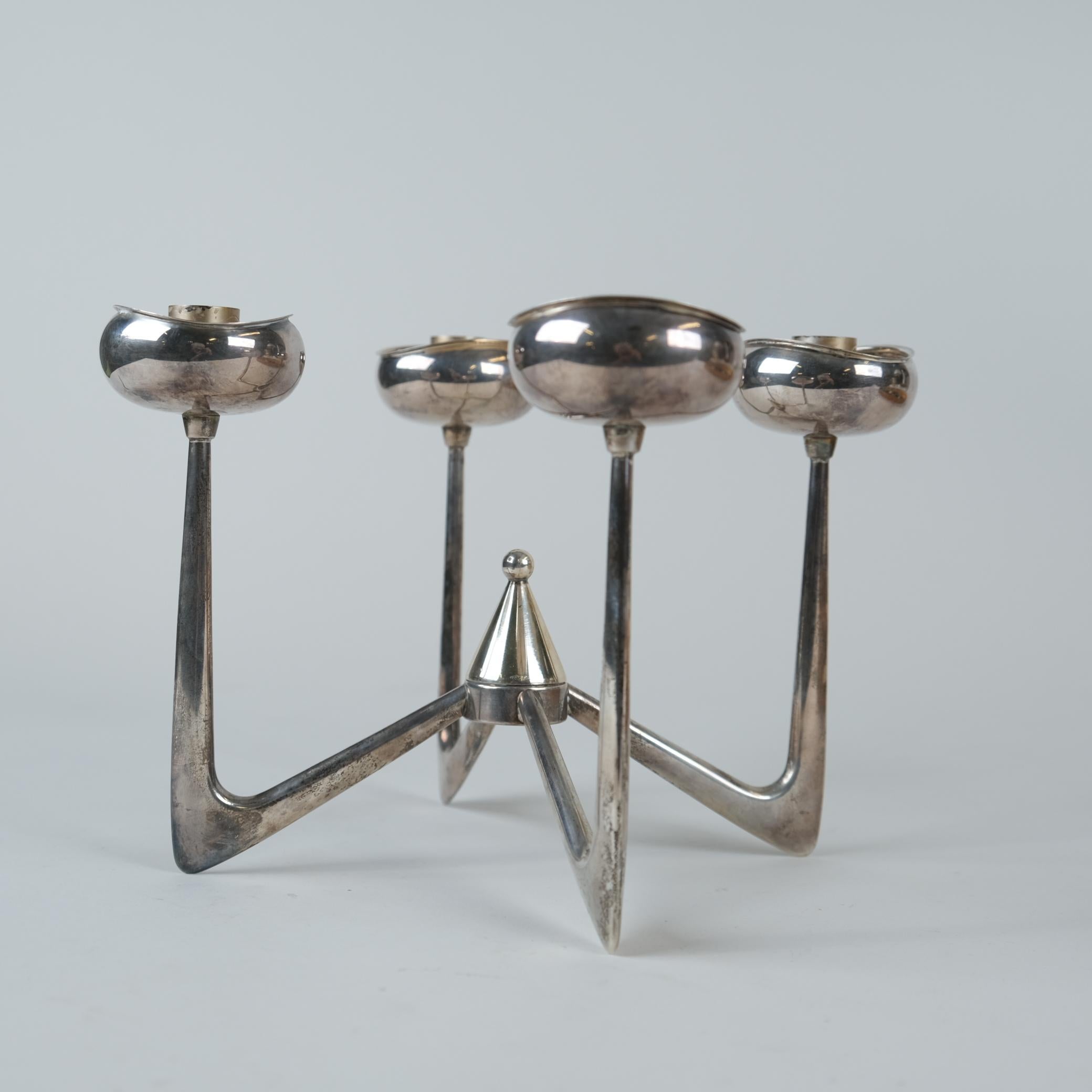 Portacandele dall'aspetto esotico e futuristico in argento massiccio disegnato da Anna Greta Eker. Questo pezzo presenta quattro basi per candele. Inoltre, la parte centrale è staccabile e può essere utilizzata per spegnere le candele (vedi foto).