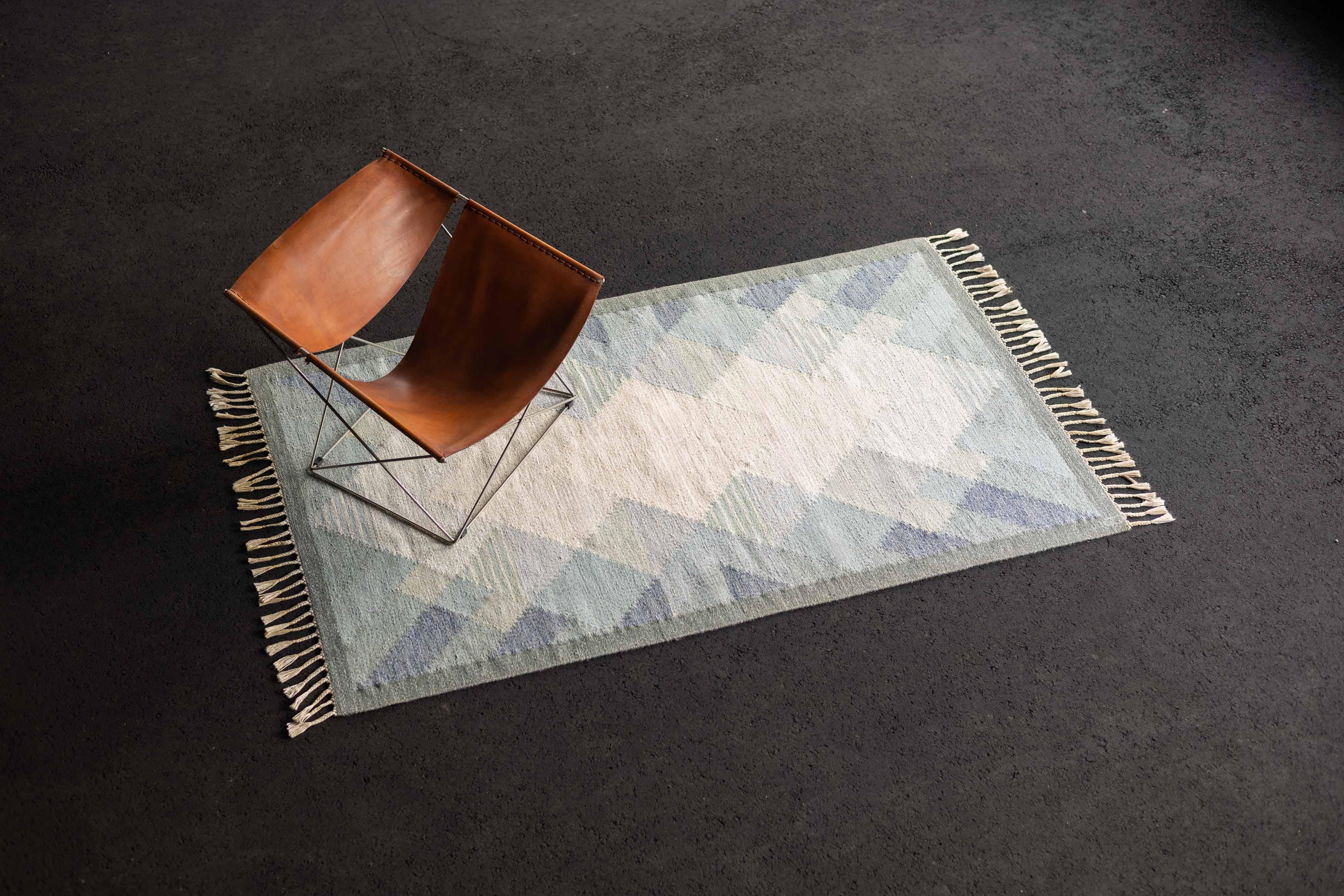 Very nice carpet designed by Anna Johanna Angstrom made in her own workshop in Sweden in 1960. This carpet is made of wool and has a beautiful geometric diamond pattern. It has this blue/green hue with beige tones and frills on the short ends.