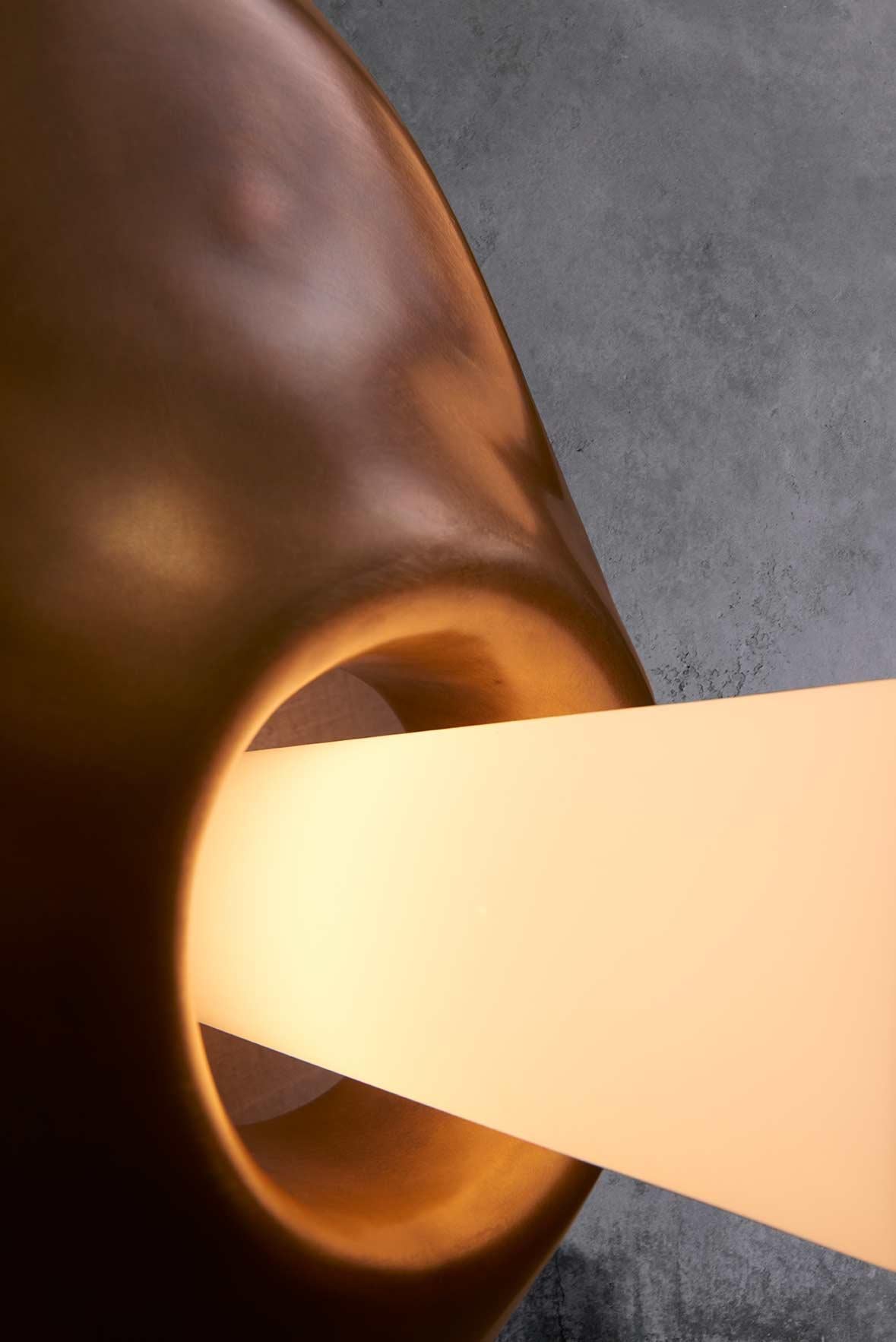 La sculpture en argile est coulée en bronze, le verre soufflé à la main est ensuite ajouté pour compléter cette forme lumineuse sculpturale. Disponible sous forme d'applique ou de suspension. Montré ici comme une applique.

Matériaux : Bronze,