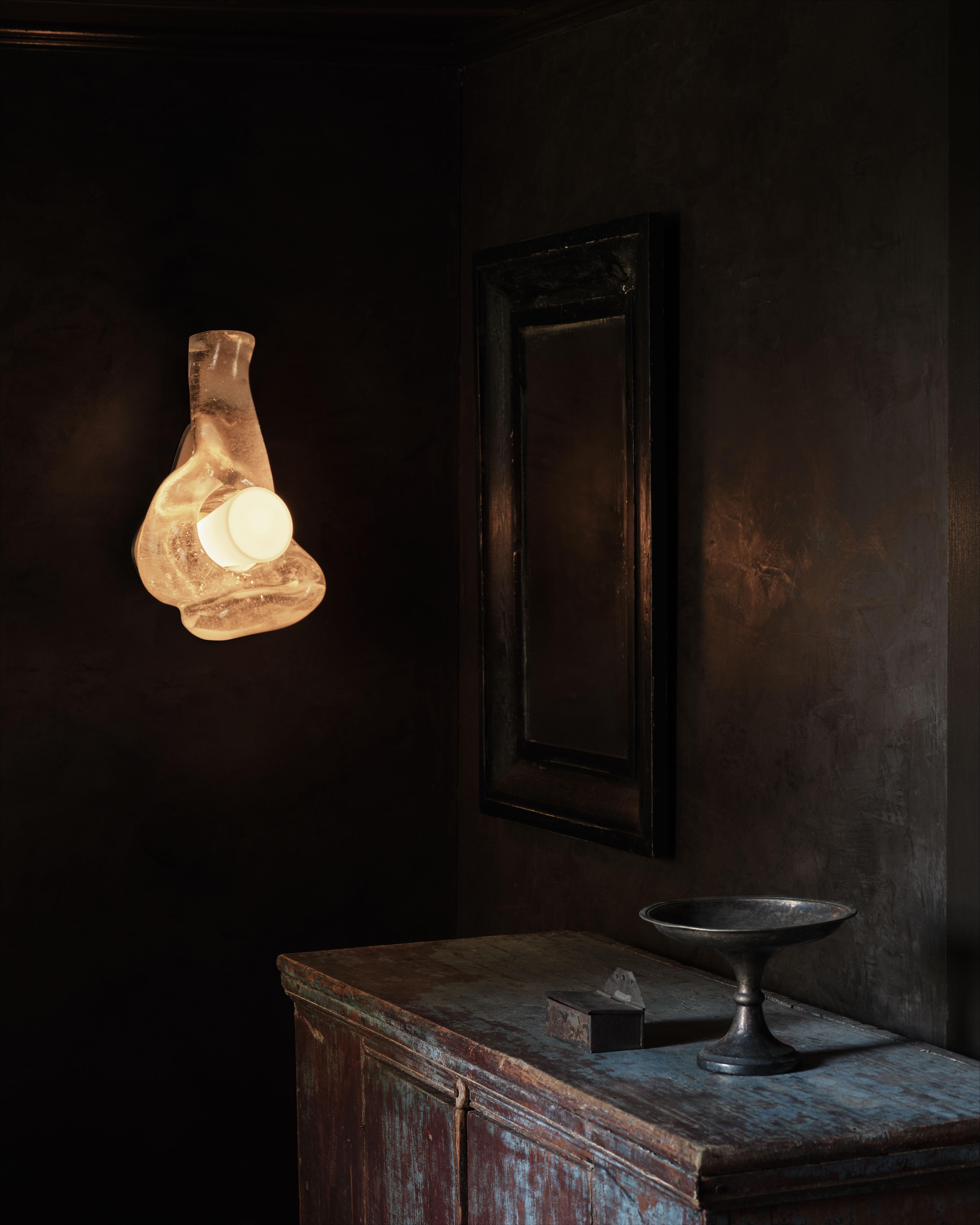 Crystal clear molten glass is poured into a graphite mold to create the sculptural body of the sconce, which is pierced by a hand-blown white glass cone and mounted to a bronze backplate armature.

Materials: Cast Bronze + Cast Glass

Dimensions: