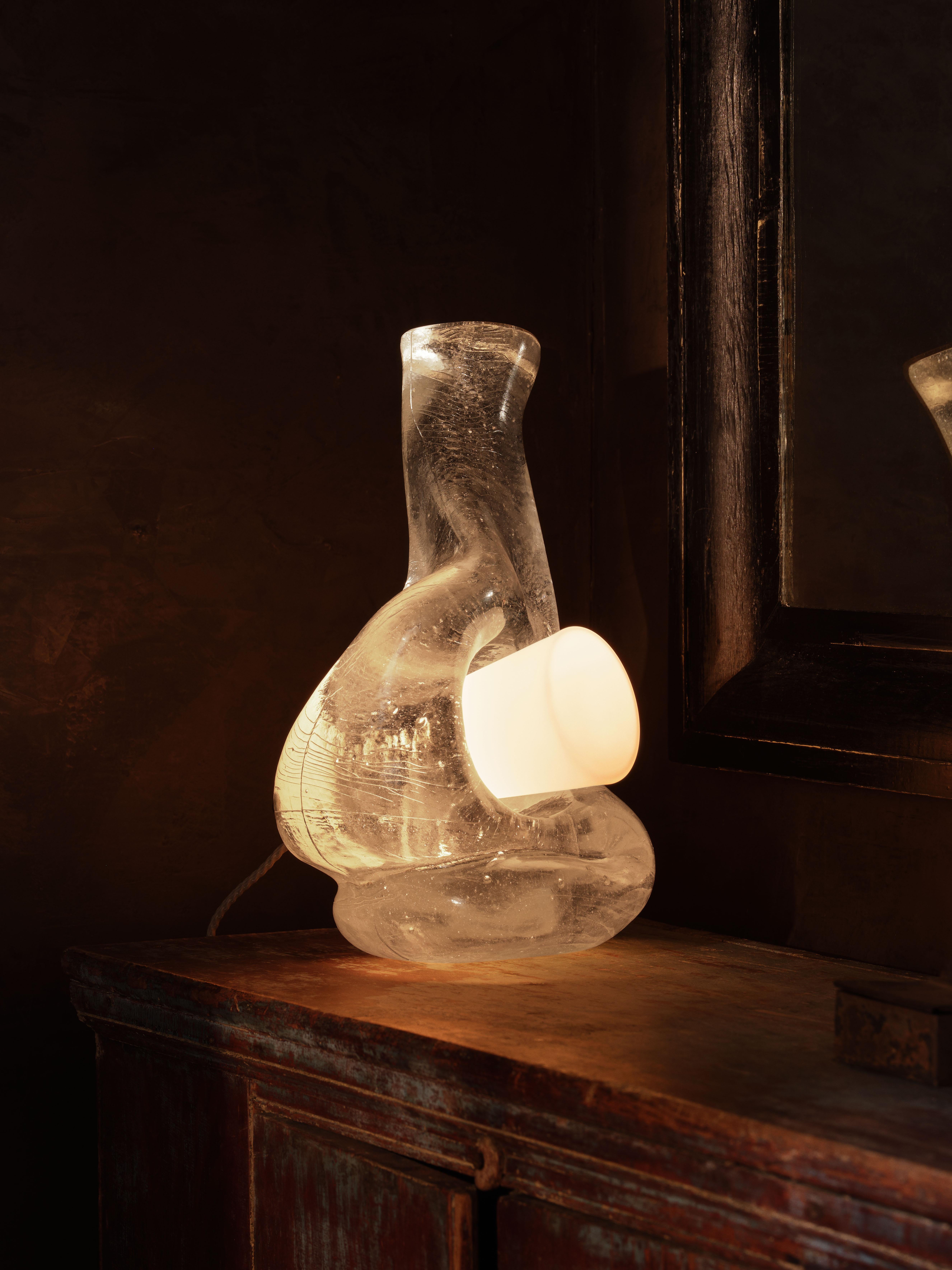 Kristallklares, geschmolzenes Glas wird in eine Graphitform gegossen, um den skulpturalen Körper der Leuchte zu formen, der von einem mundgeblasenen weißen Glaskegel durchbrochen und an einer Bronzearmatur befestigt wird.

MATERIALIEN: Gussglas,