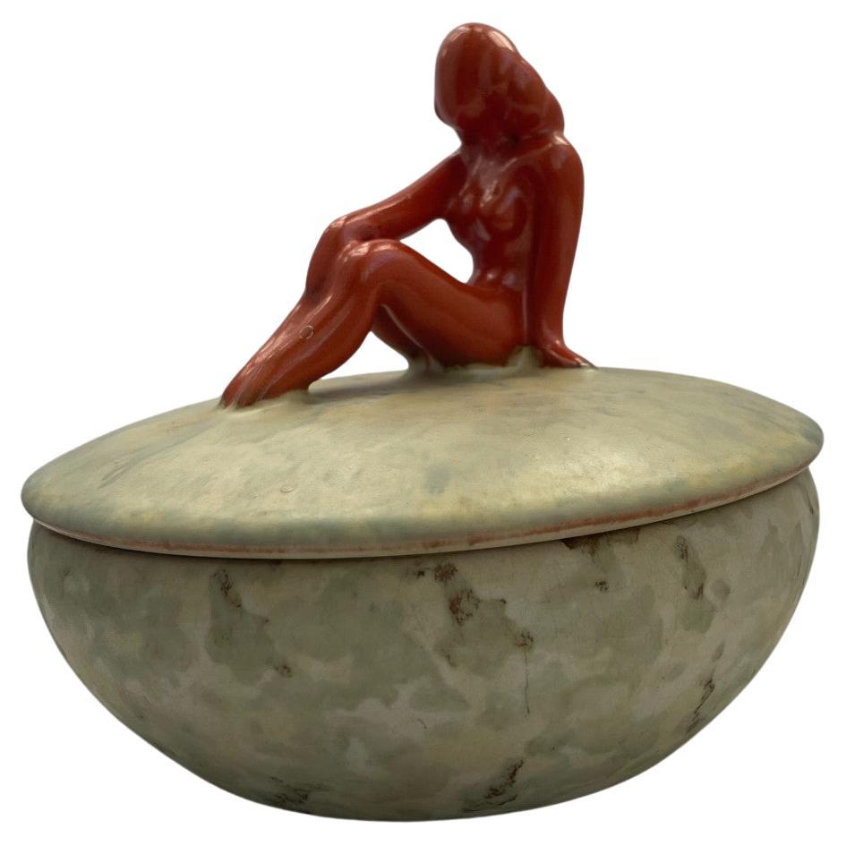 Elegant lidded ceramic bowl designed by Anna-Lisa Thomson for Upsala-Ekeby, Sweden, circa 1930s.
The piece features a softly rounded bowl in a mottled matte glaze of pale green and beige tones, crowned with a striking glossy red figurine of a seated
