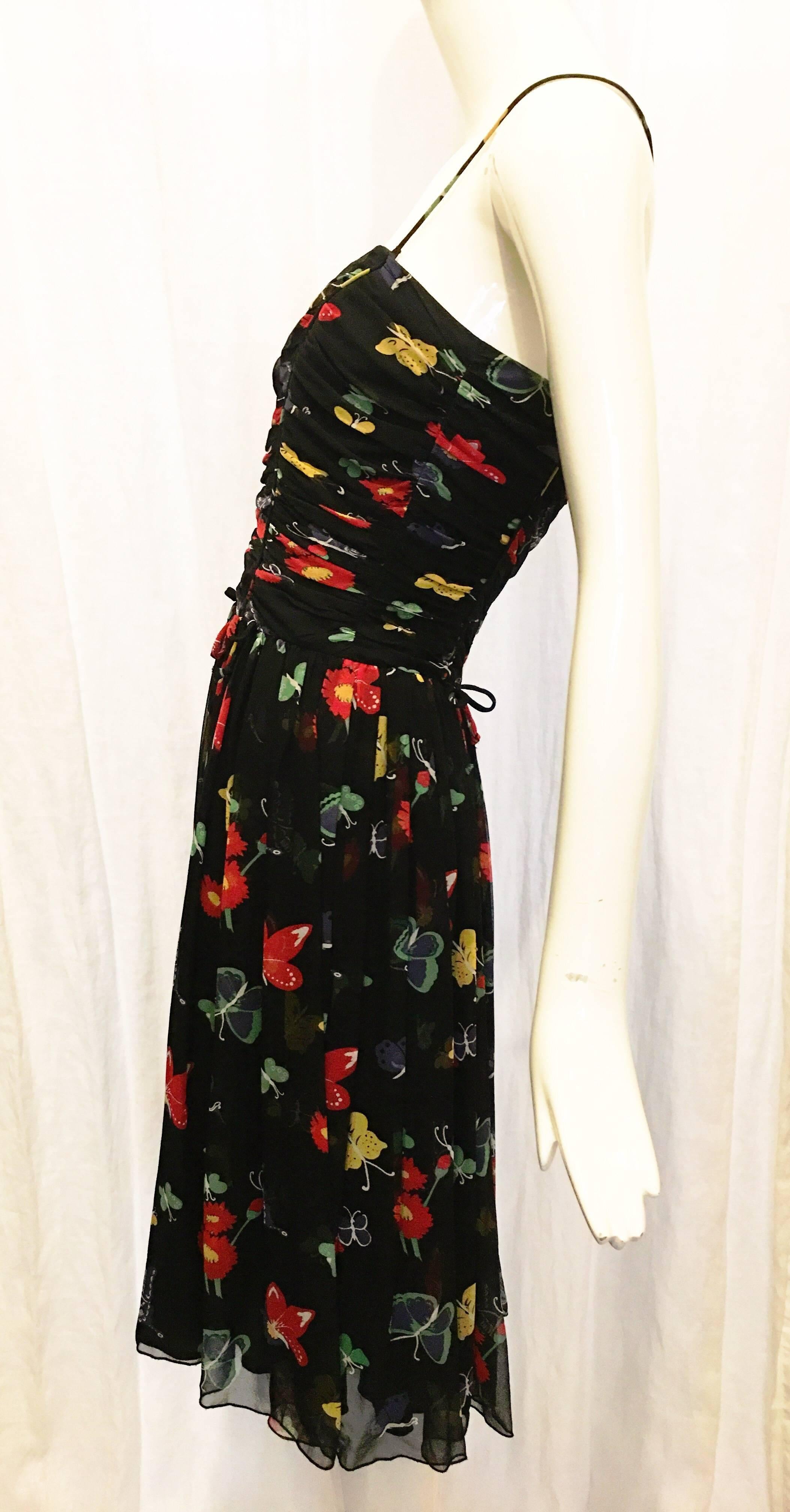 Black ruched bodice dress with allover flower print. Spaghetti straps that attach with buttons for the option of wearing the dress as strapless. Ties at waist at front and back. Zips at back with hook and eye closure. Moves well. A perfect sundress