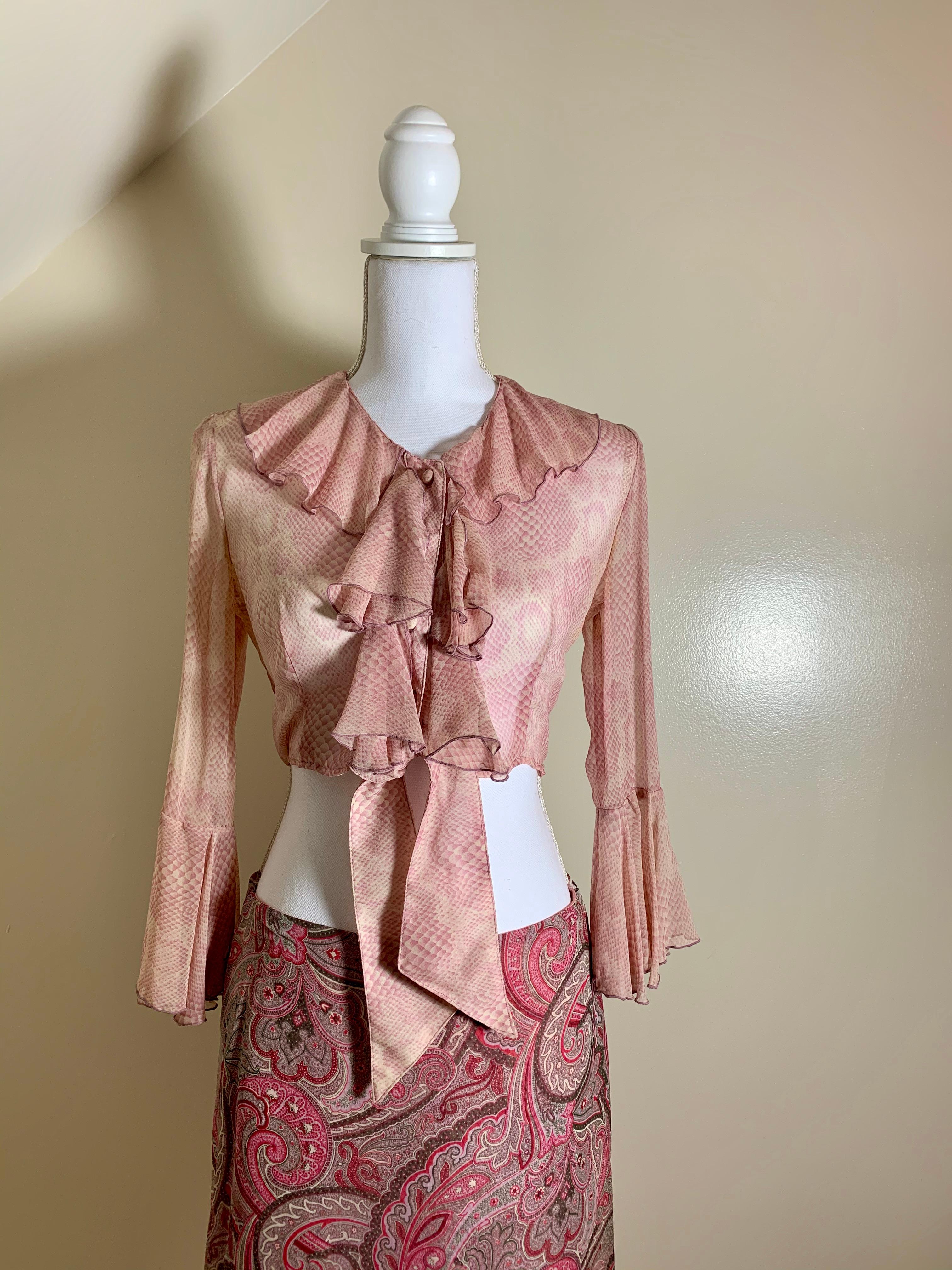 An early 1990s Anna Sui Paisley and Snakeskin print two-piece ensemble.

The midriff baring top is in a sheer pink snakeskin printed fabric, with a cascading ruffled neckline and collar, front fabric covered buttons, and long ruffled sleeves.
 
The