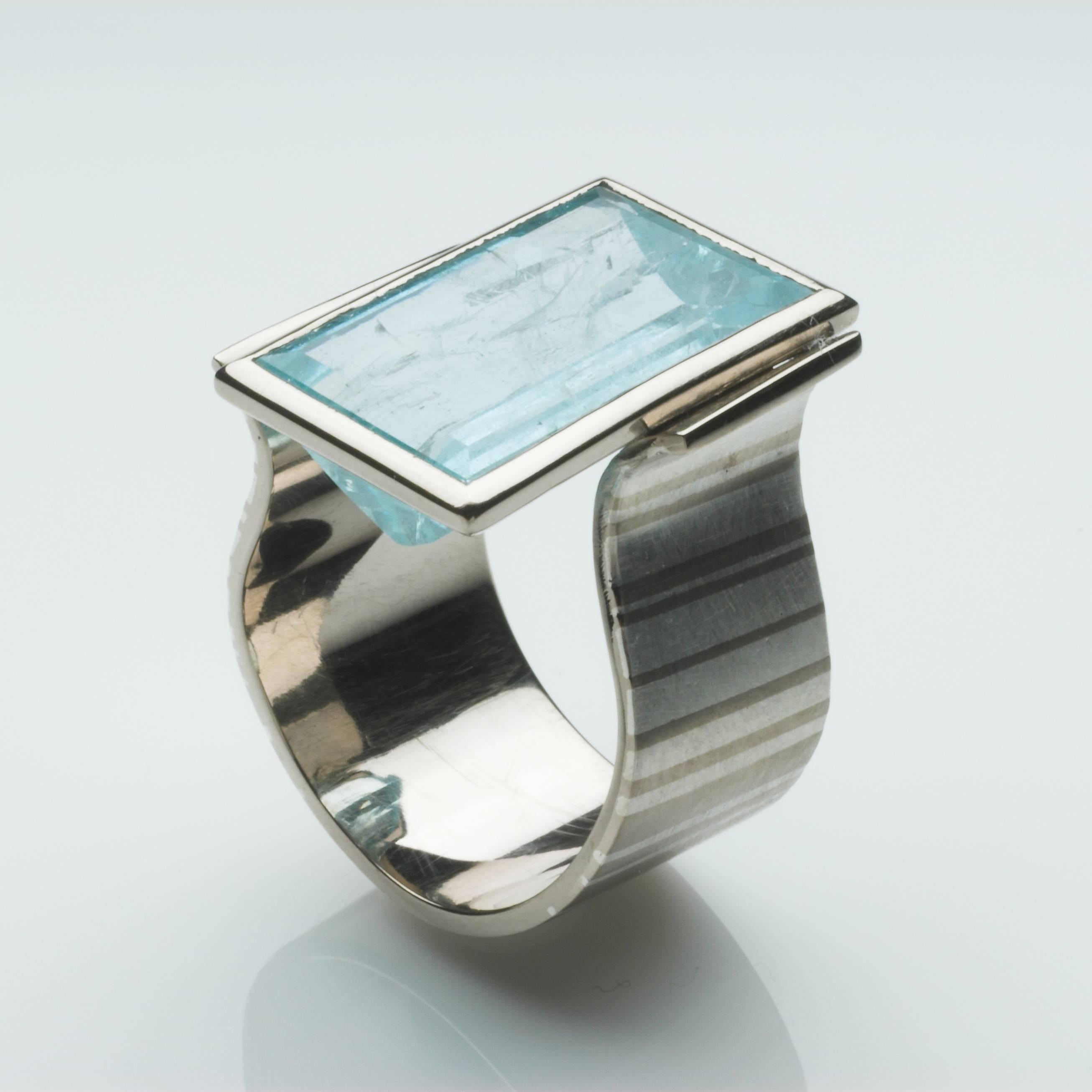 Barcode ring in 18ct white gold, with a fused fine silver inlay forming contrasting varying width stripes, set with a large rectangular aquamarine. The stripes in the ring shank are echoed in the cut of the stone.
UK ring size: O