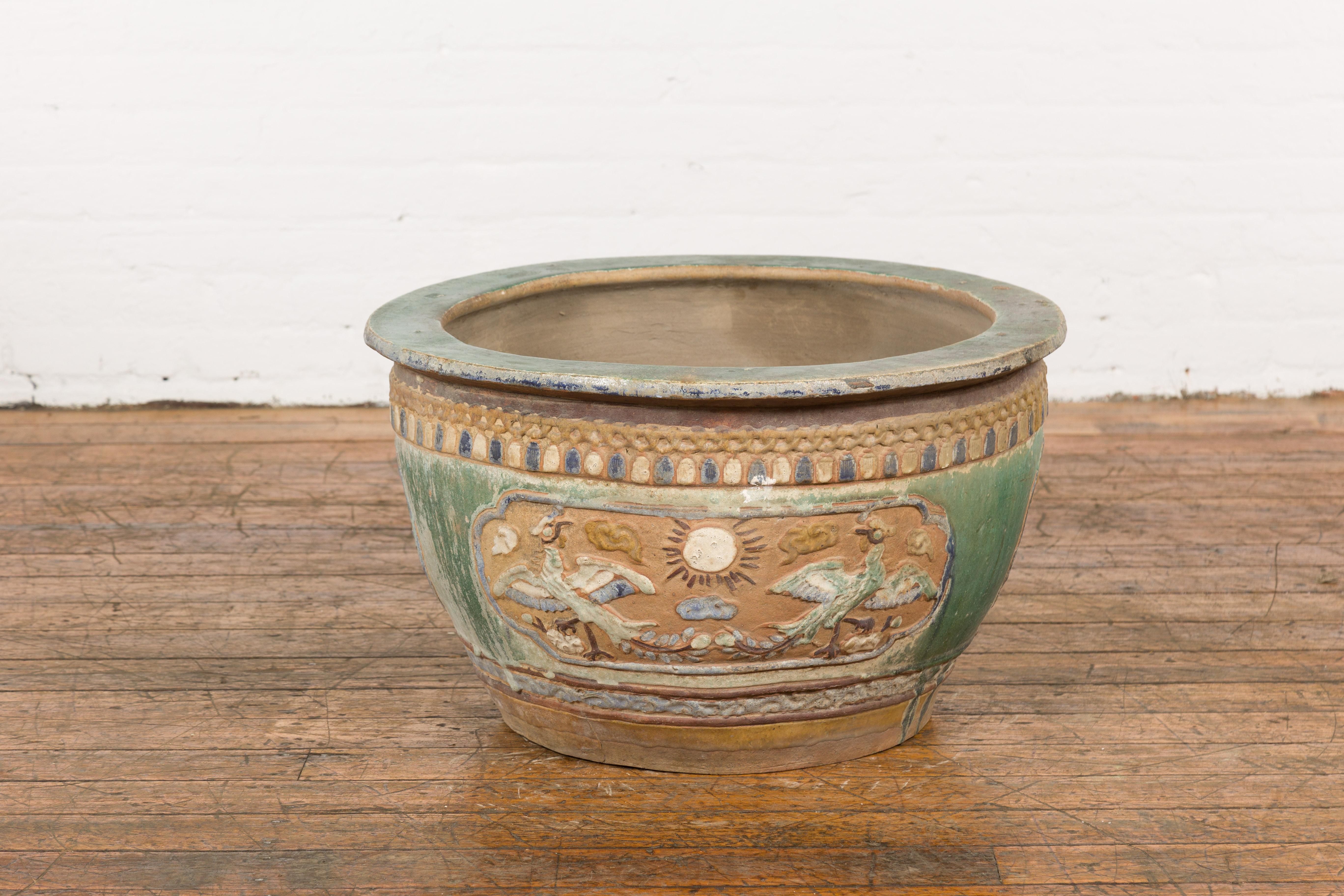 An antique 19th century Annamese green, blue and ocher glazed planter from Vietnam with birds, sun, scrolling clouds, trees and deer motifs, as well as a distressed patina. Immerse yourself in the rich cultural heritage of Vietnam with this antique