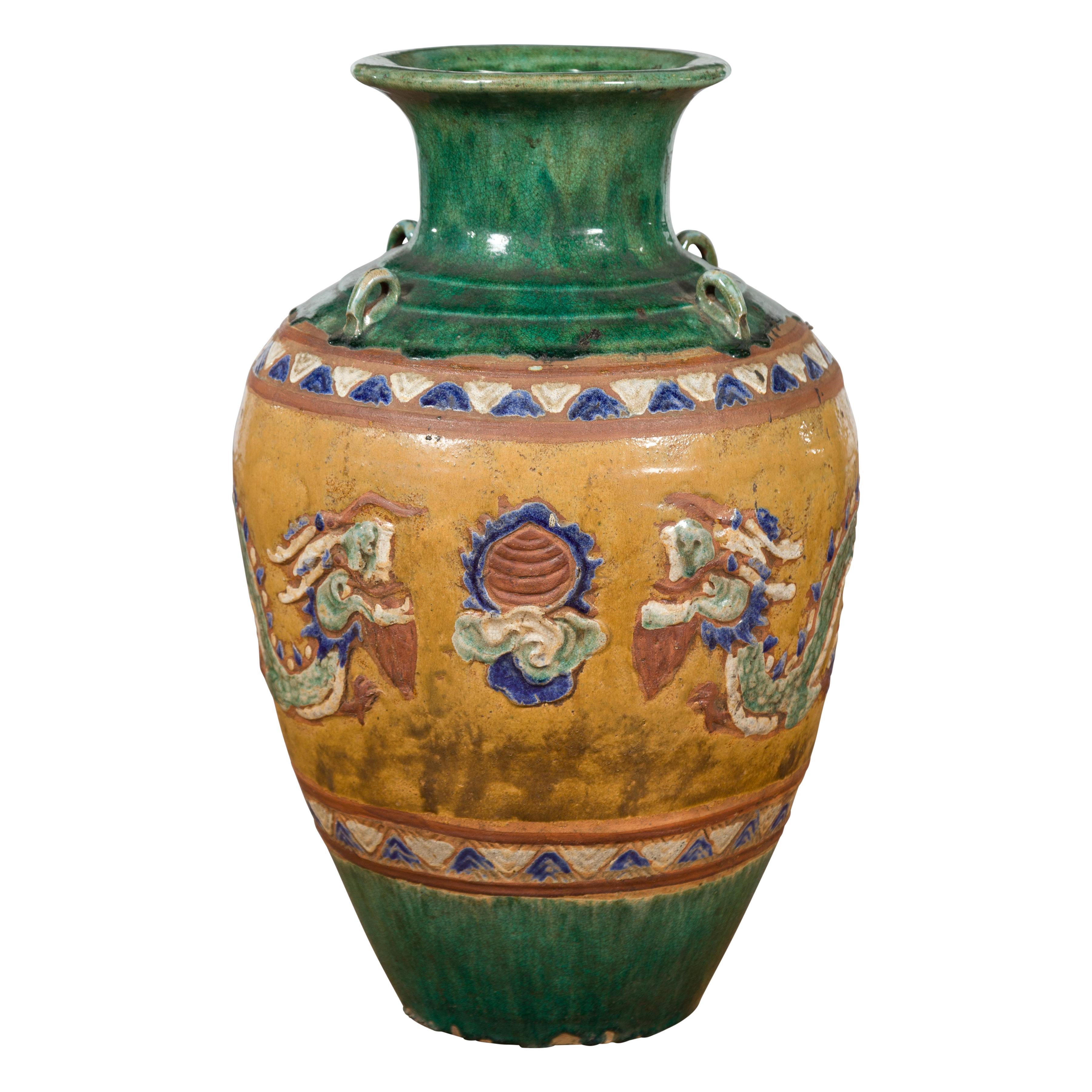 An antique Vietnamese Annamese green water jar from the 19th century, with raised dragon motifs, blue, brown and yellow accents and petite loop handles. Created in Vietnam during the 19th century, this green glazed Annamese Martaban vase is adorned
