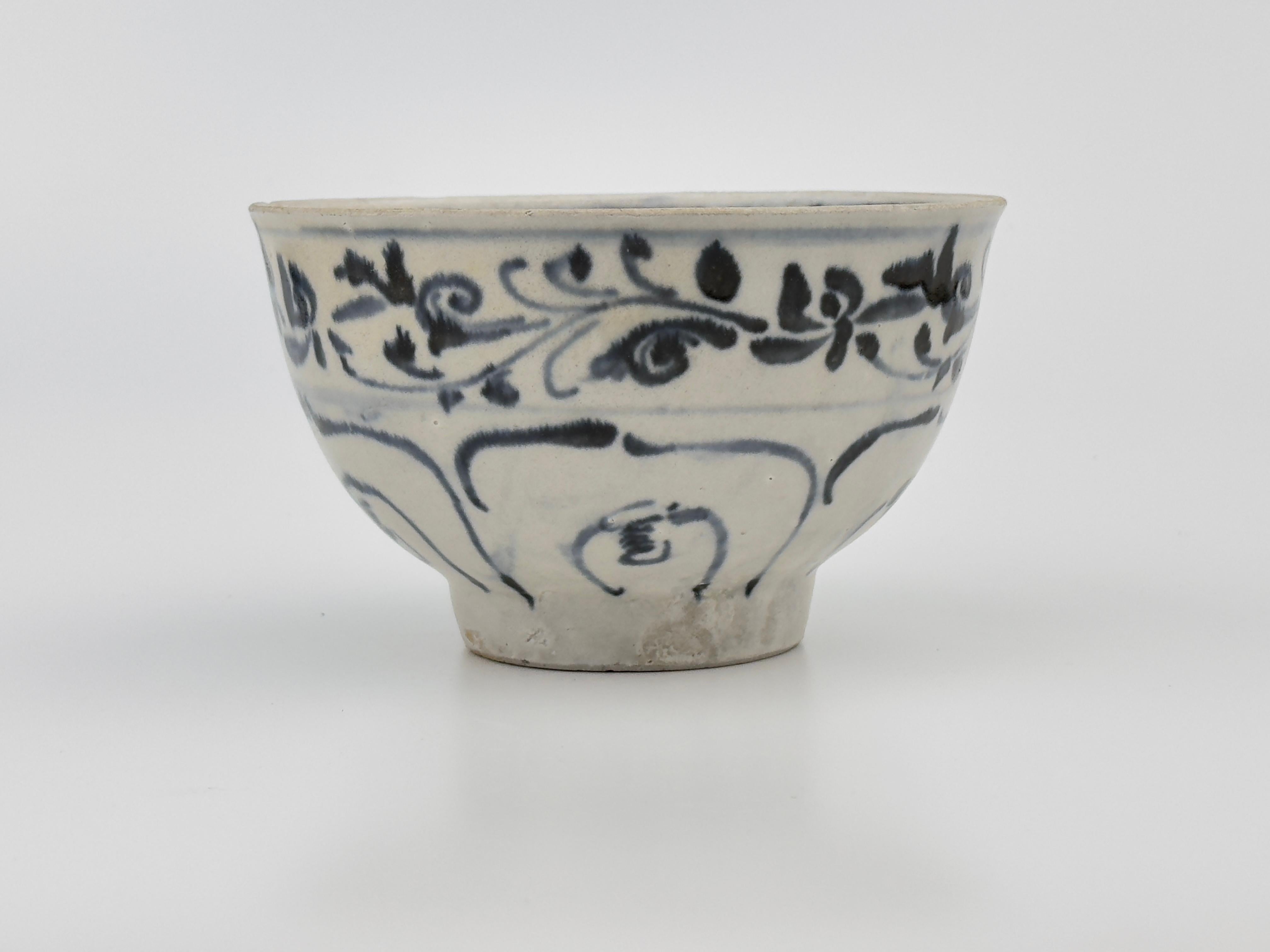 The bowl's design features fluid, dynamic brushstrokes typical of Annamese pottery, where cobalt blue underglaze was used to create intricate patterns before a clear glaze was applied. The artwork, with its foliage and floral motifs, suggests a