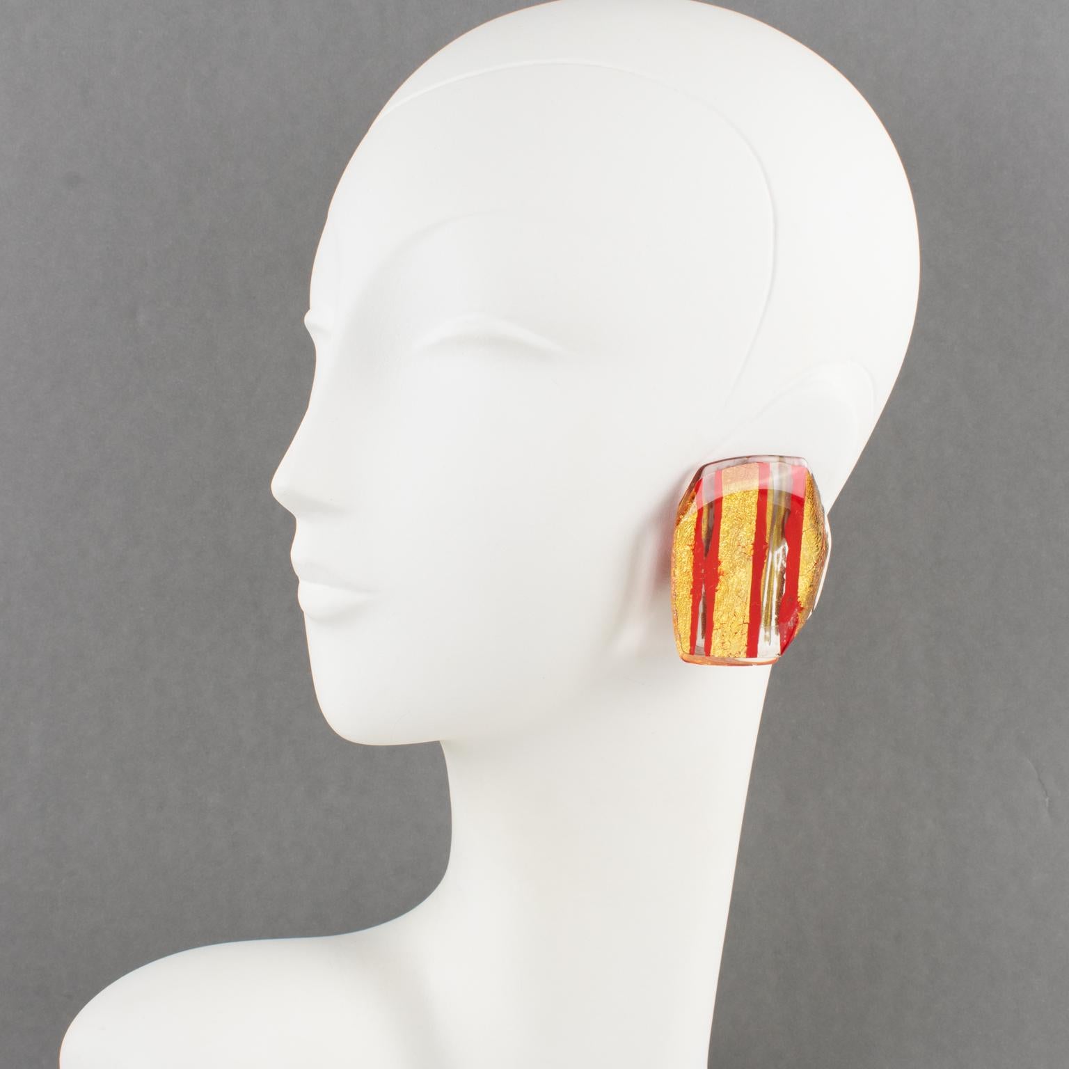These lovely Anne and Frank Vigneri Lucite clip-on earrings feature an oversized dimensional geometric design, all faceted and carved. The design boasts crystal clear Lucite with a red striped pattern and gold metallic foil inclusions. There is no